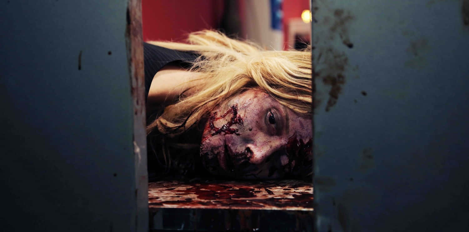 Scary Zombie 桌布 壁紙 — 一名血跡斑斑的金髮女子透過生鏽的金屬縫隙窺視，表情驚恐。