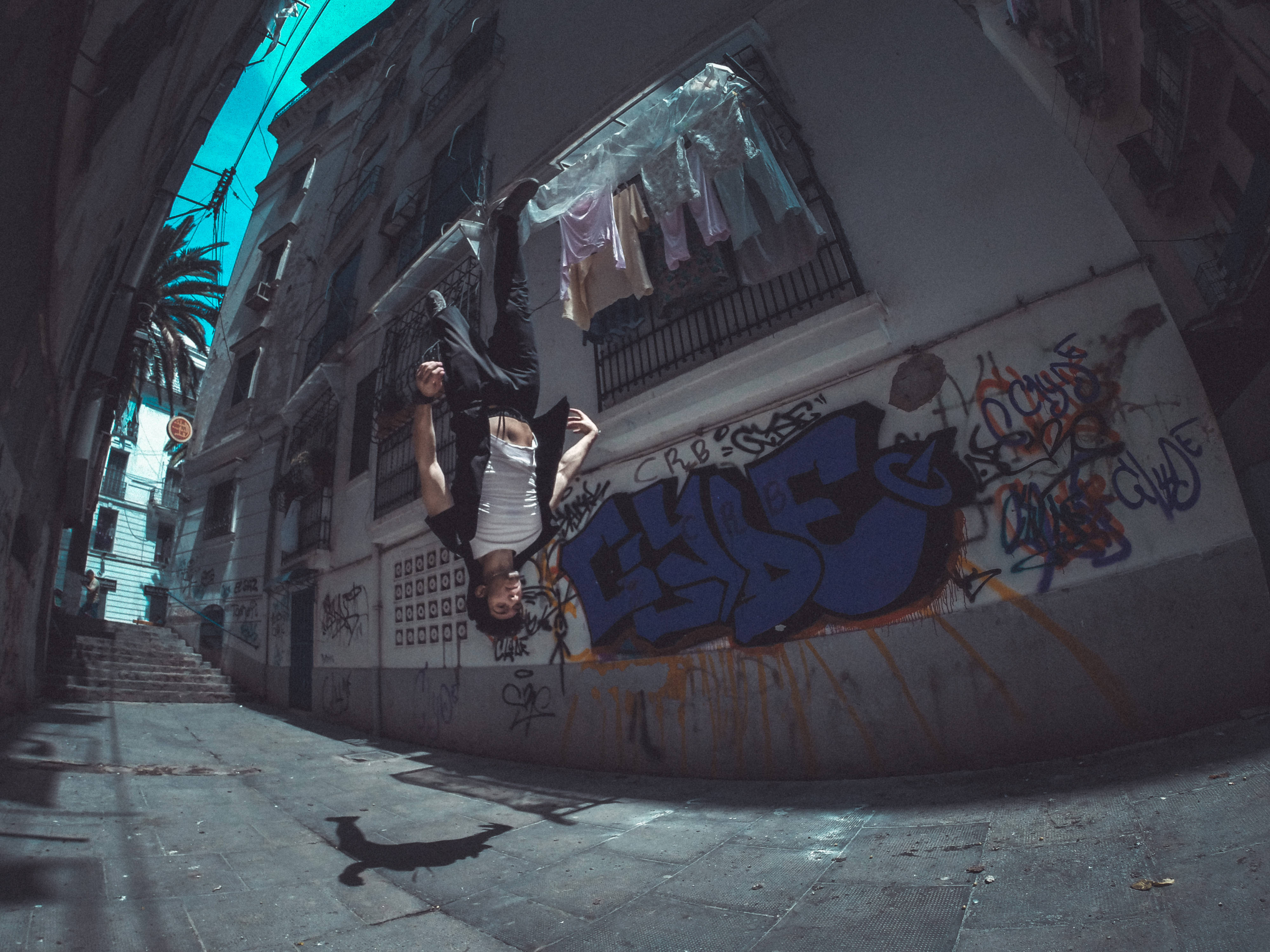 Parkour 桌布 壁紙 — 一名街頭舞者在充滿塗鴉的小巷中，在鮮豔的藍天下表演挑戰地心引力的翻轉。