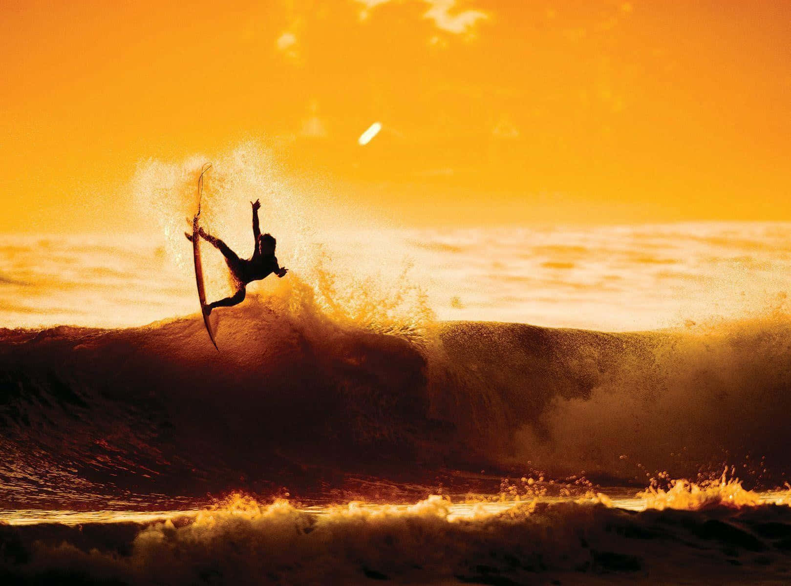 surfing 桌布 壁紙 — 一名衝浪者在半空中從海浪上躍起，金色的夕陽光芒以溫暖的色調沐浴著海洋。