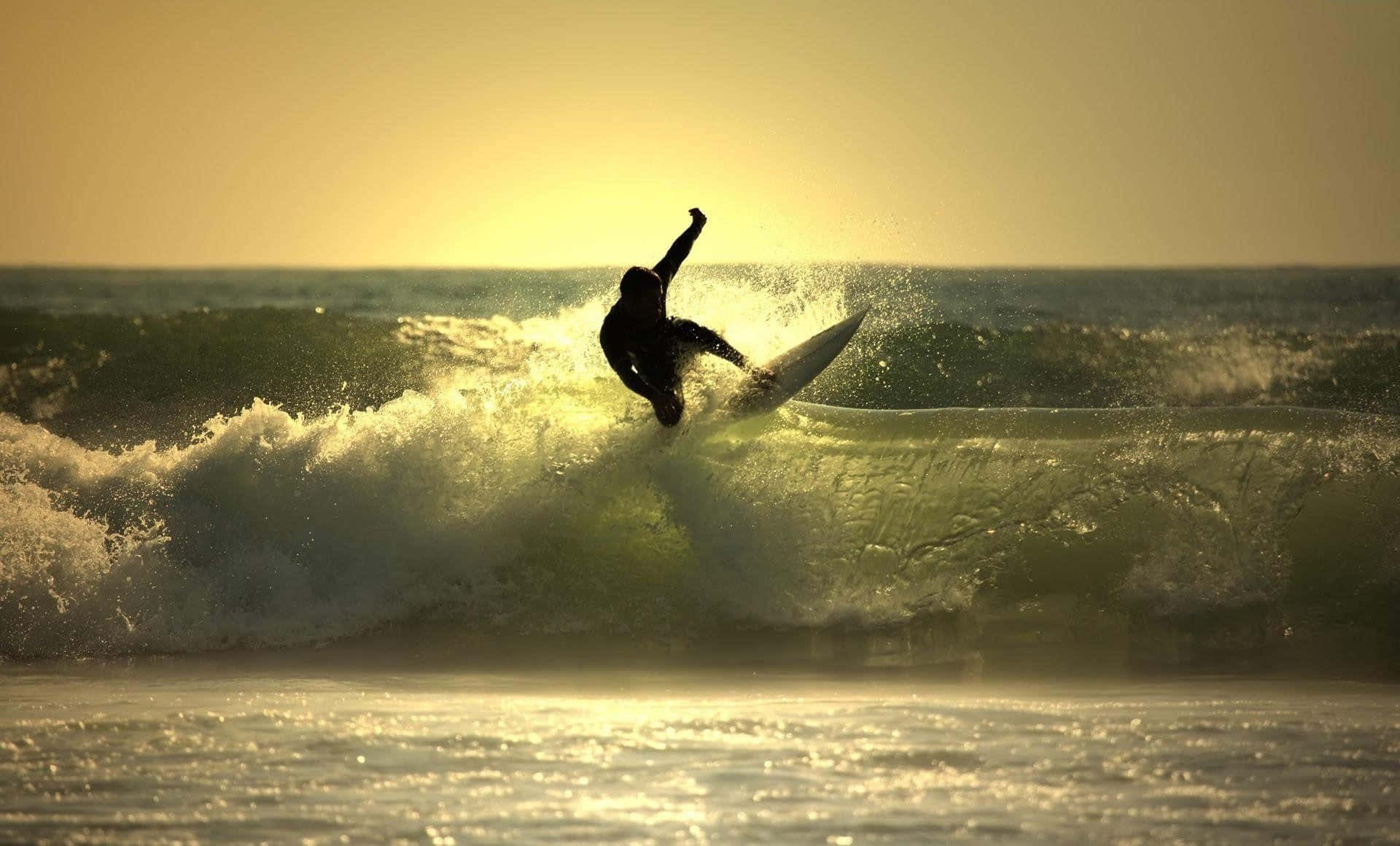 surfing 桌布 壁紙 — 一名衝浪者在日落時分乘著金色海浪，一隻手臂高舉向發光的天空。