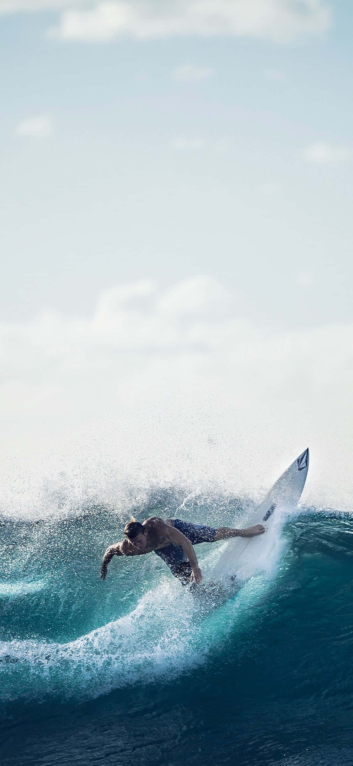 Surfing iPhone 桌布 壁紙 — 一名衝浪者在明亮的天空和散落的雲朵下，駕馭著強勁的藍綠色海浪。