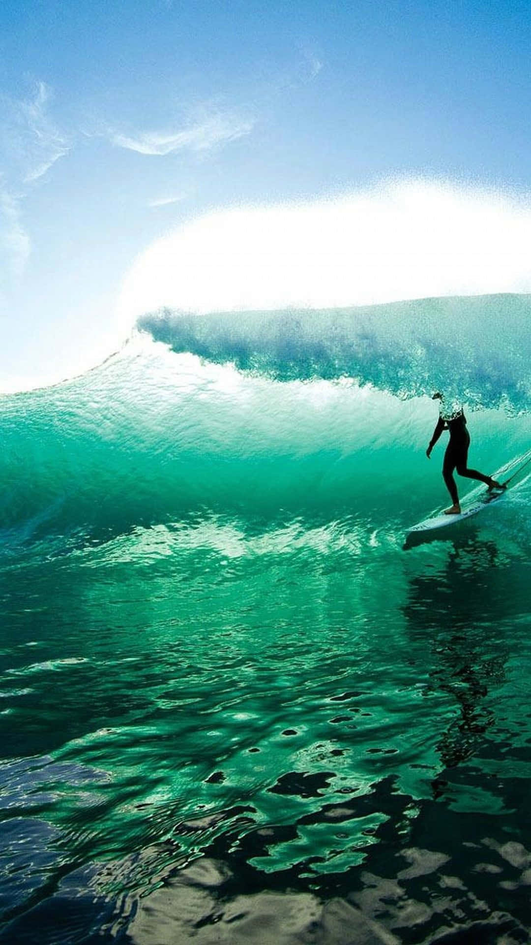 Surfing iPhone 桌布 壁紙 — 一名衝浪者在晴朗的藍天下騎乘巨大的藍綠色海浪，陽光穿透浪管。
