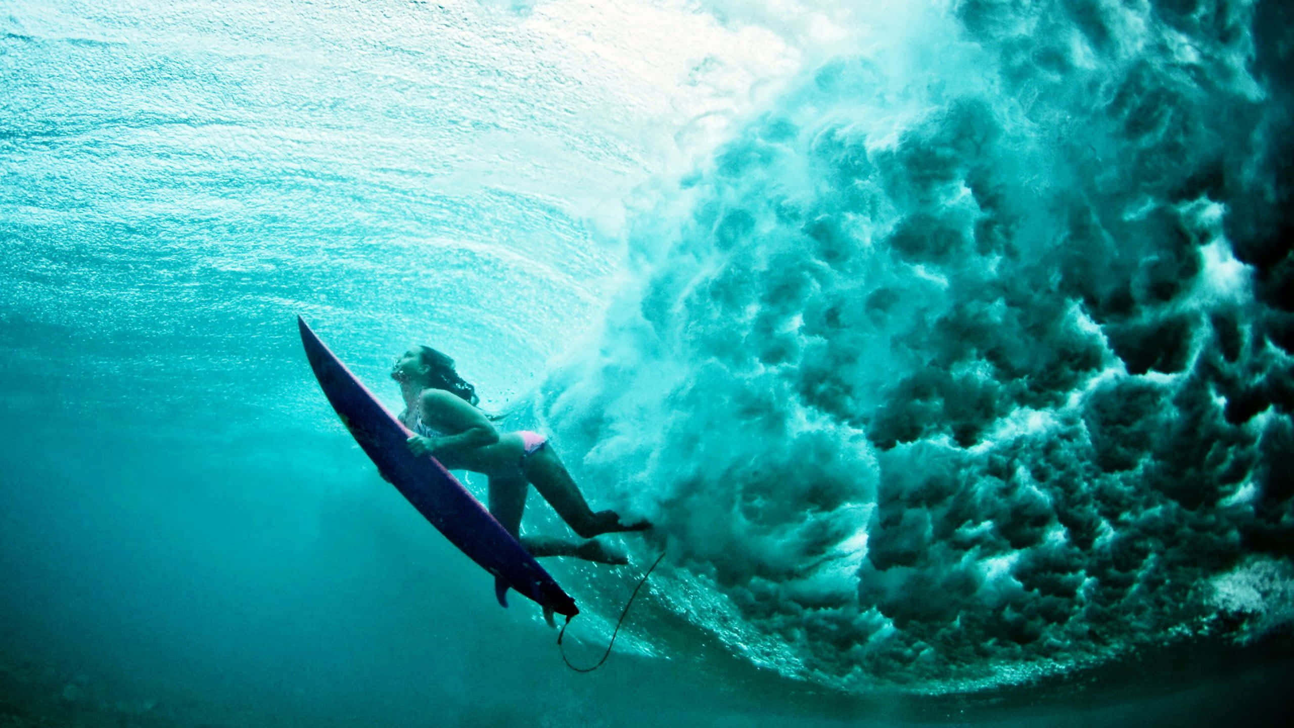 surfing 桌布 壁紙 — 一名衝浪者在水中滑行，穿過一個巨大的藍綠色波浪在頭頂捲曲的動態海洋鏡頭。
