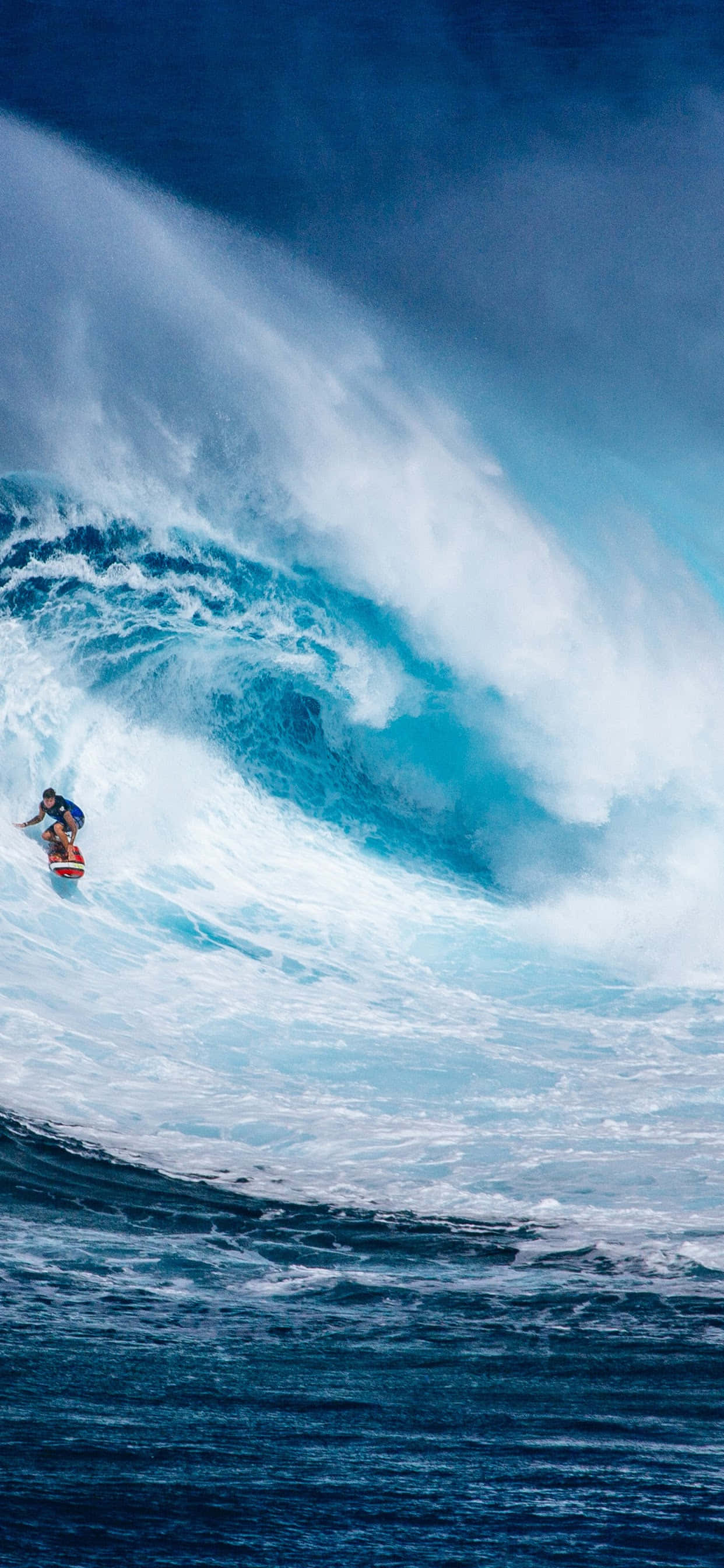 Surfing iPhone 桌布 壁紙 — 一名衝浪者在深藍色天空下騎乘巨大的藍綠色海浪，周圍水花飛濺。