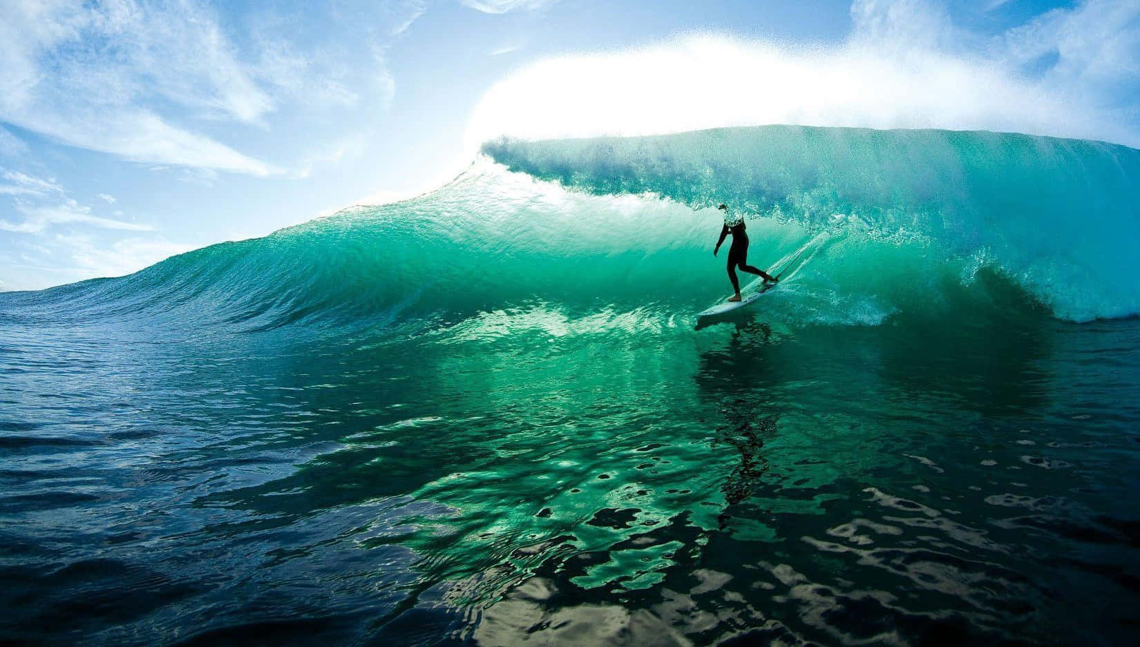 surfing 桌布 壁紙 — 一名衝浪者在藍天白雲下乘著巨大的藍綠色海浪。