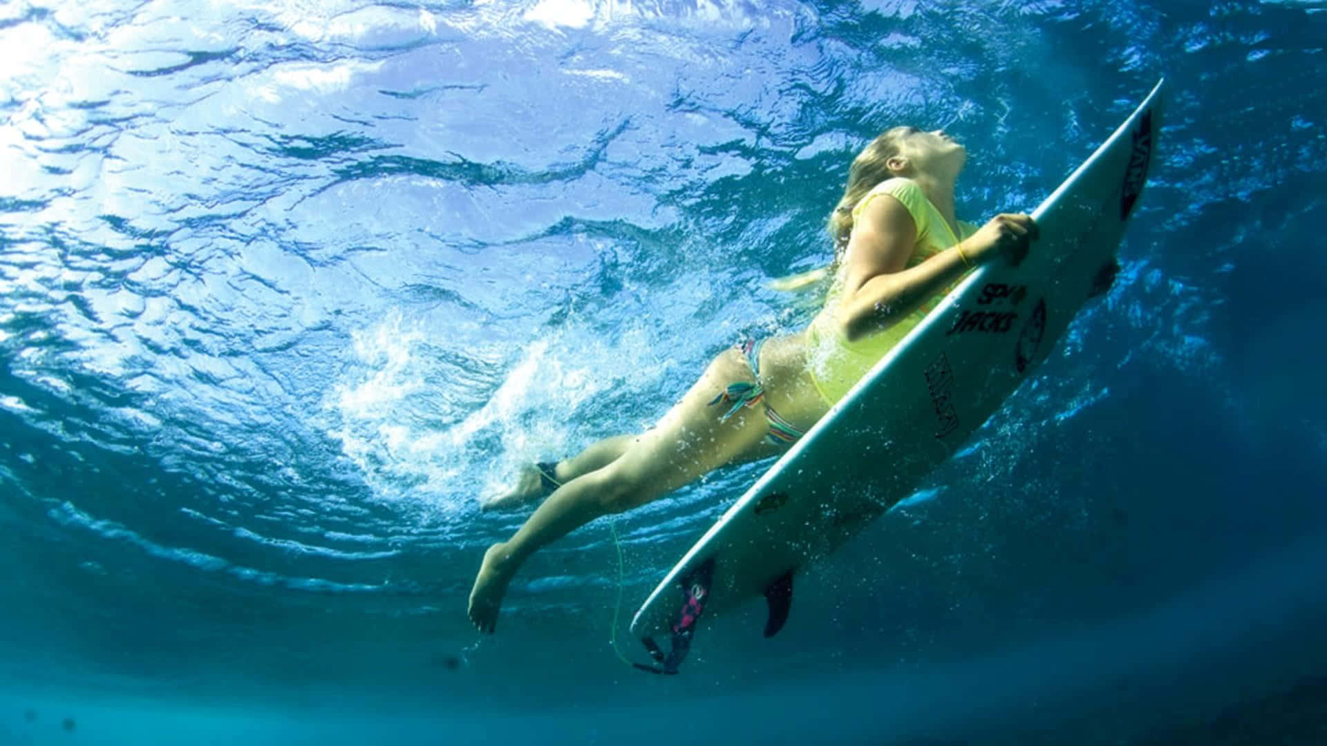 surfing 桌布 壁紙 — 一名衝浪者拿著衝浪板在水下滑行，陽光透過碧綠的海浪照射進來。
