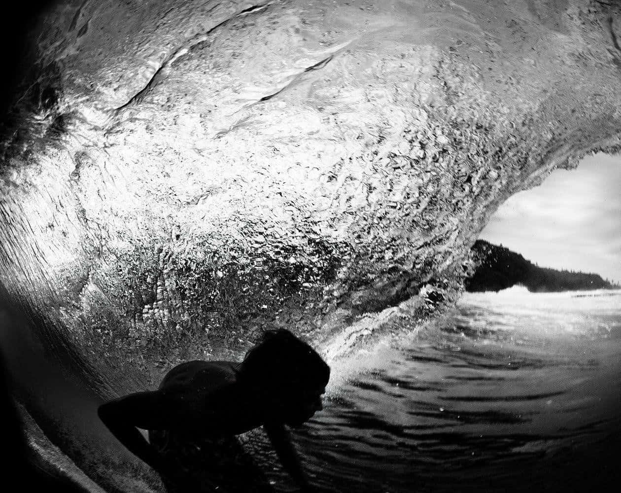 surfing 桌布 壁紙 — 一名衝浪者的剪影在巨大的捲曲海浪下滑行，以戲劇性的黑白捕捉。
