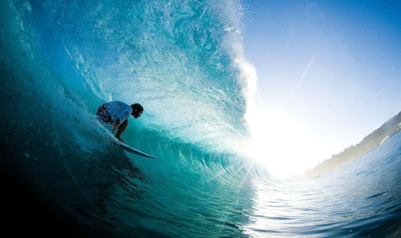 surfing 桌布 壁紙 — 一名衝浪者騎乘巨大的藍綠色海浪，陽光穿過浪管照射。