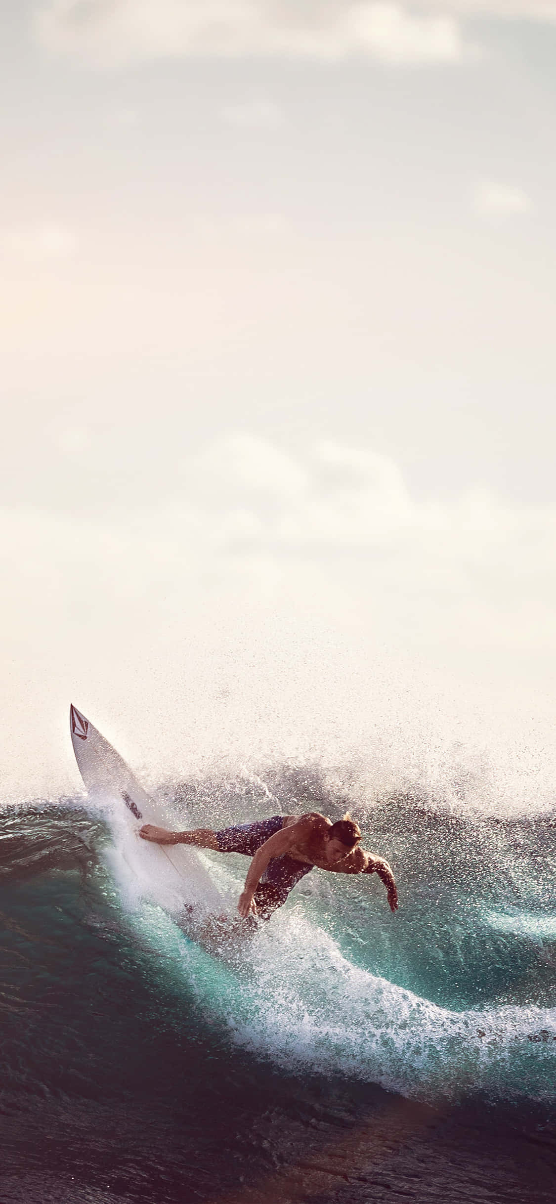 Surfing iPhone 桌布 壁紙 — 一名衝浪者騎在碧綠色的海浪上，水花四濺，夕陽在他身後落下。