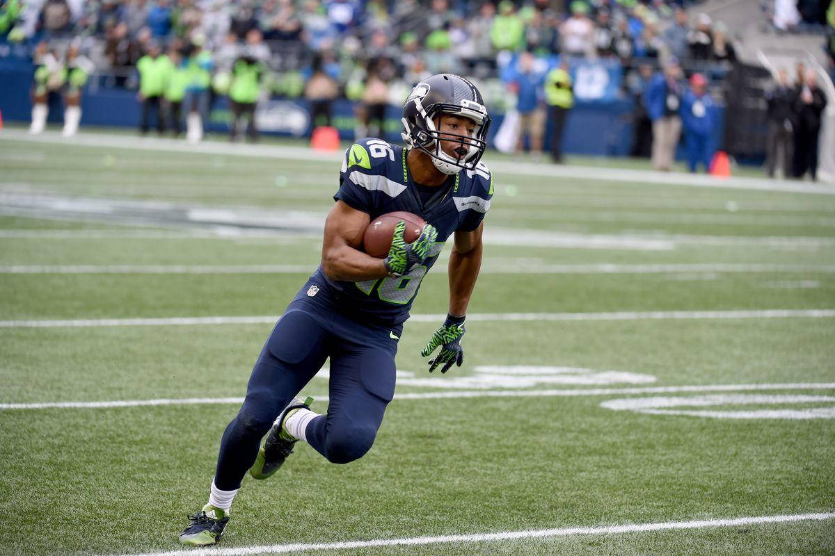 Seattle Seahawks 桌布 壁紙 — 一名西雅圖海鷹隊美式足球員在日間比賽中抱著球衝過綠色球場。