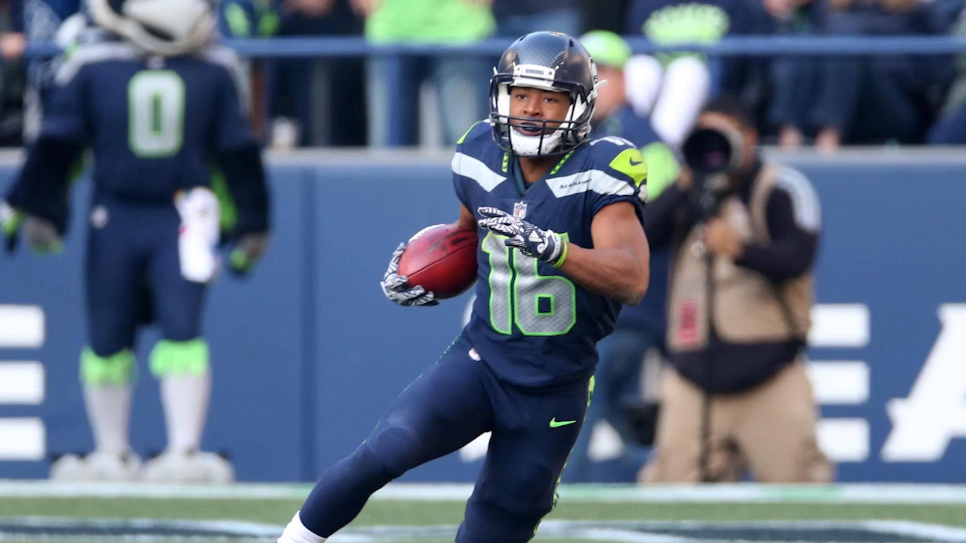 Seattle Seahawks 桌布 壁紙 — 一名西雅圖海鷹隊美式足球員身穿海軍藍和螢光綠色制服，在日間比賽中持球衝刺。