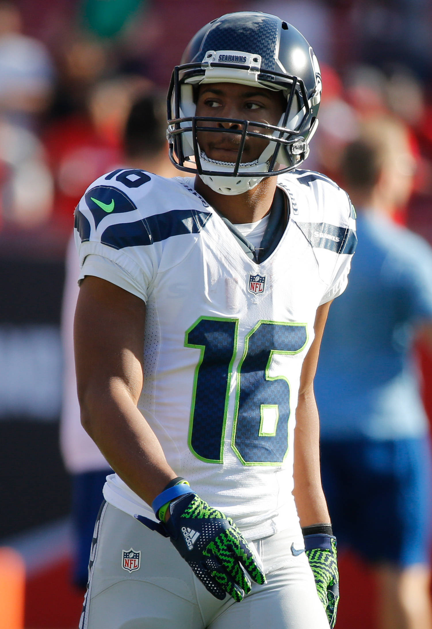Seattle Seahawks 桌布 壁紙 — 一名西雅圖海鷹隊美式足球員身穿白色及藍綠色16號球衣，在明亮的日光下專注地站在球場上。
