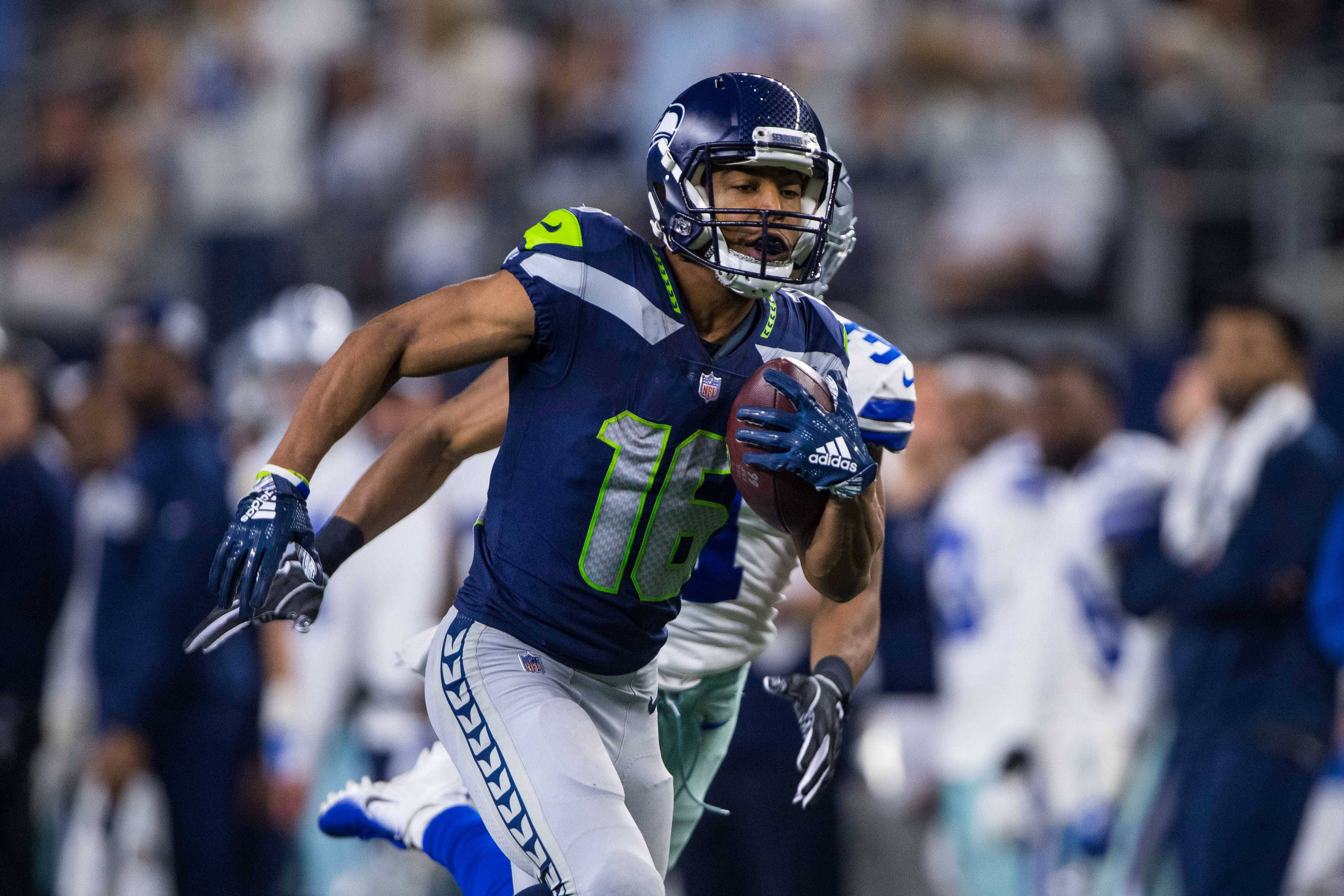 Seattle Seahawks 桌布 壁紙 — 一名西雅圖海鷹隊美式足球員身穿藍綠球衣，在夜間比賽的球場燈光下持球衝刺。