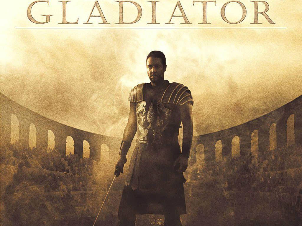Gladiator 桌布 壁紙 — 一名角鬥士莊嚴地站在塵土飛揚的羅馬競技場中，在朦朧的金色天空下手持一把劍。