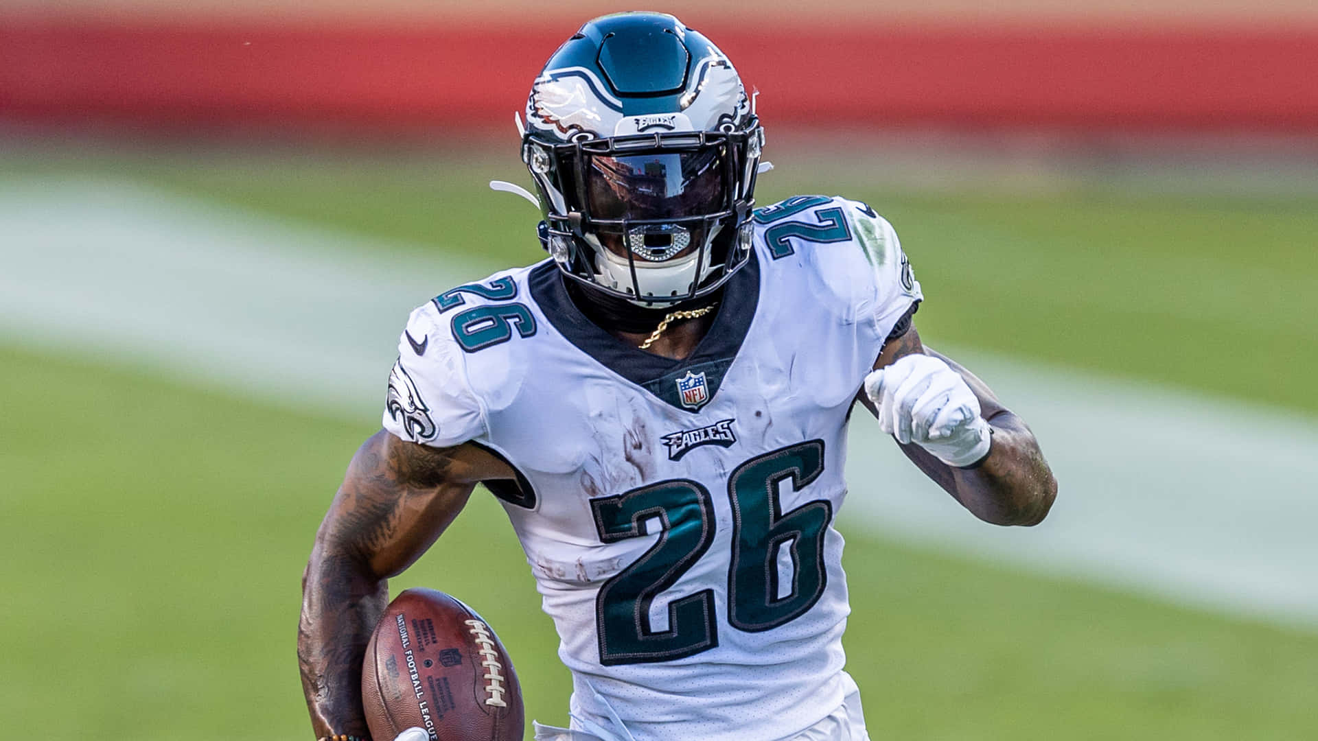 Miles Sanders 桌布 壁紙 — 一名費城老鷹隊身穿白色26號球衣的美式足球員在綠色球場上帶球衝刺。