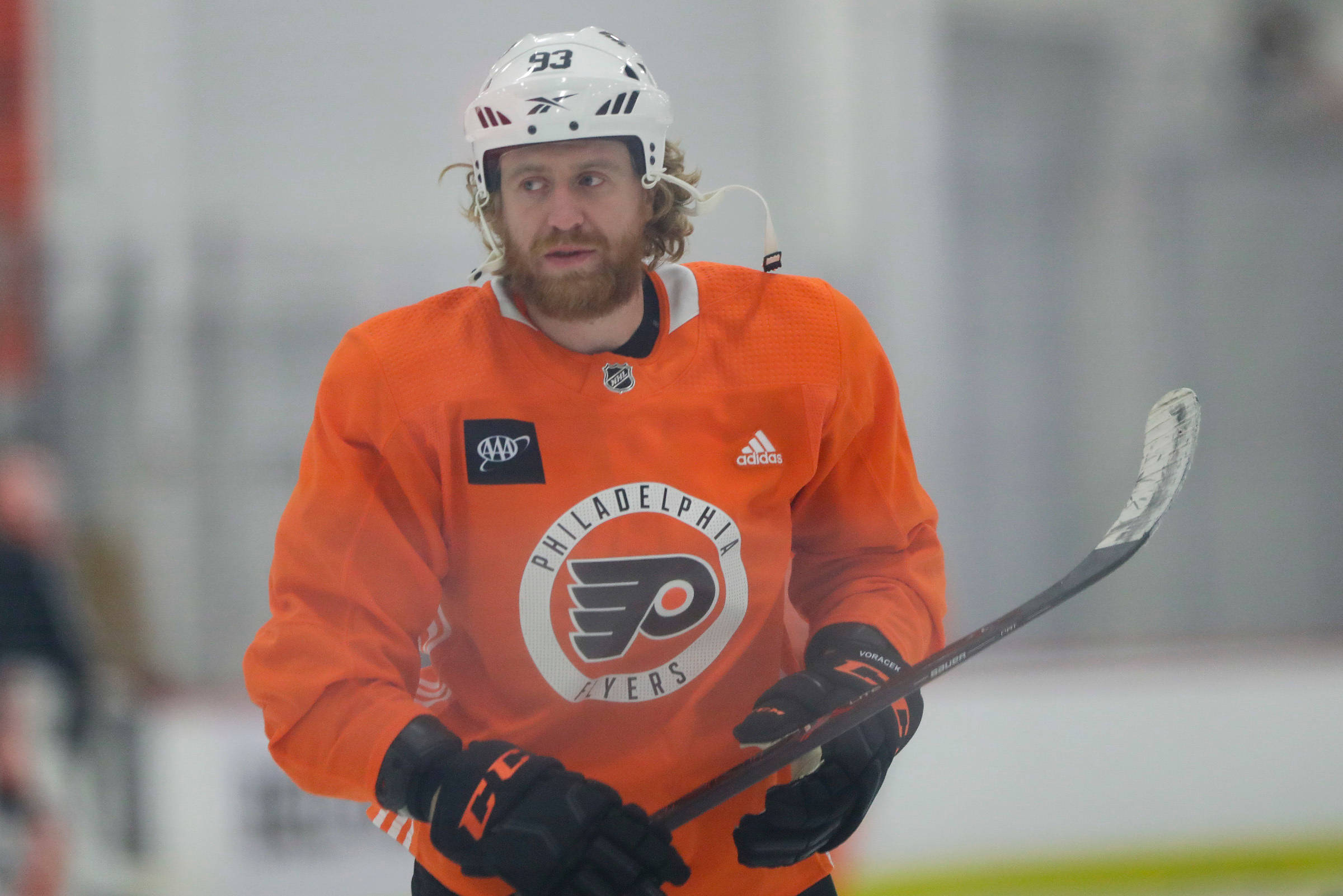 hockey 桌布 壁紙 — 一名費城飛人隊的冰球運動員，身穿橙色球衣和白色頭盔，在冰上握著球棍，眼神銳利。