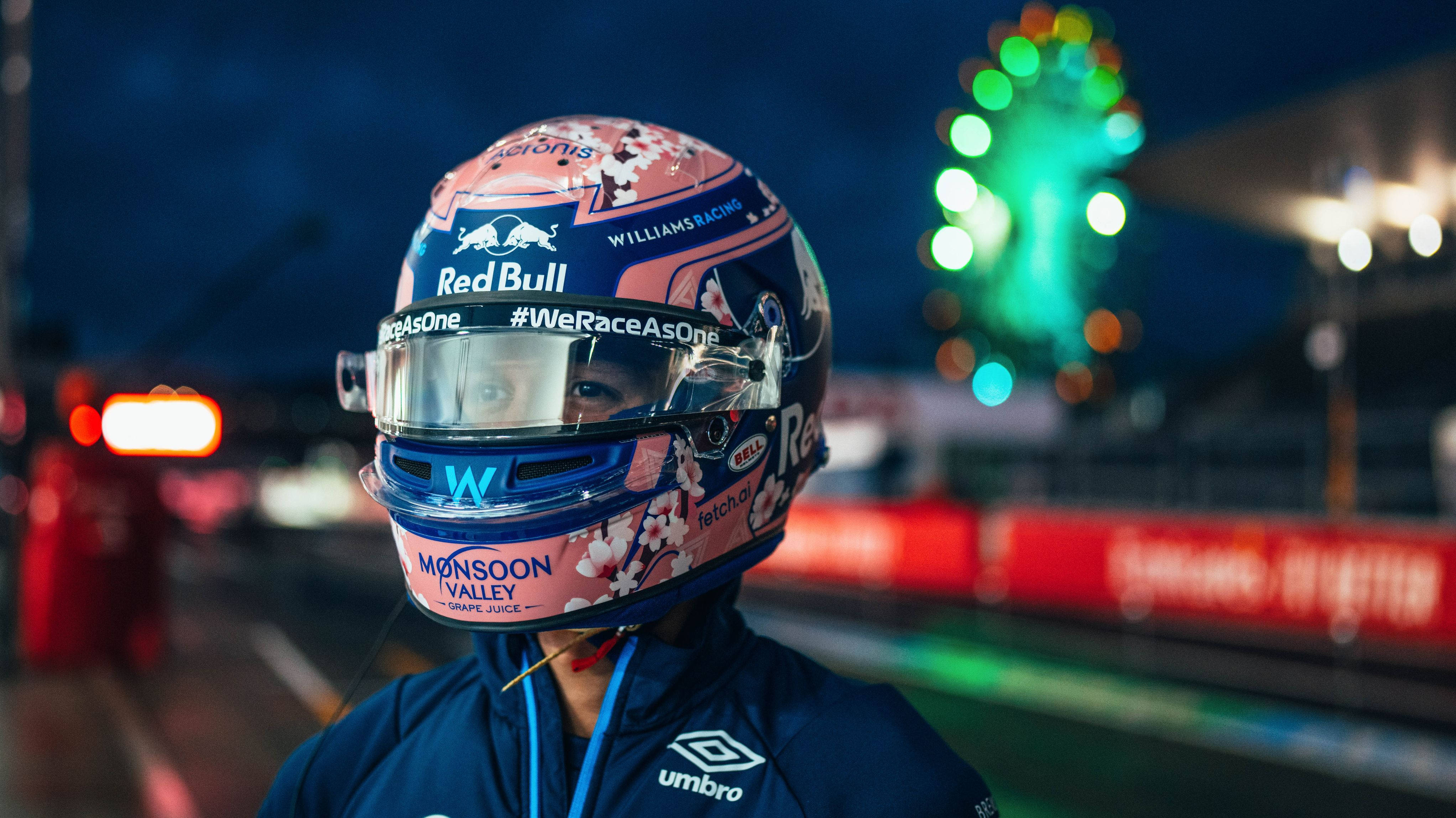 Racing 桌布 壁紙 — 一名賽車手戴著花卉頭盔，夜晚站在賽道上，背景有發光的燈光。