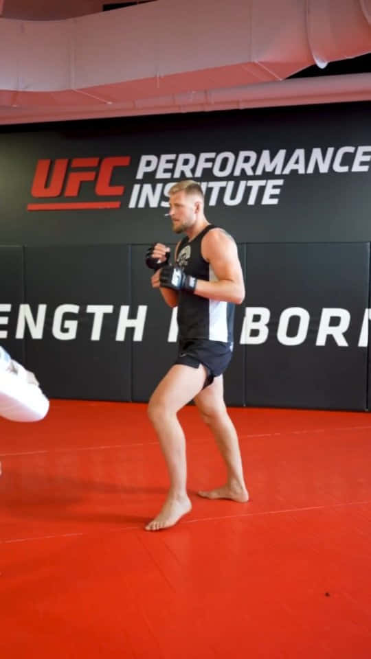 UFC 桌布 壁紙 — 一名赤腳的男性拳手穿著黑色短褲和手套，在紅色地墊的UFC Performance Institute健身房訓練。
