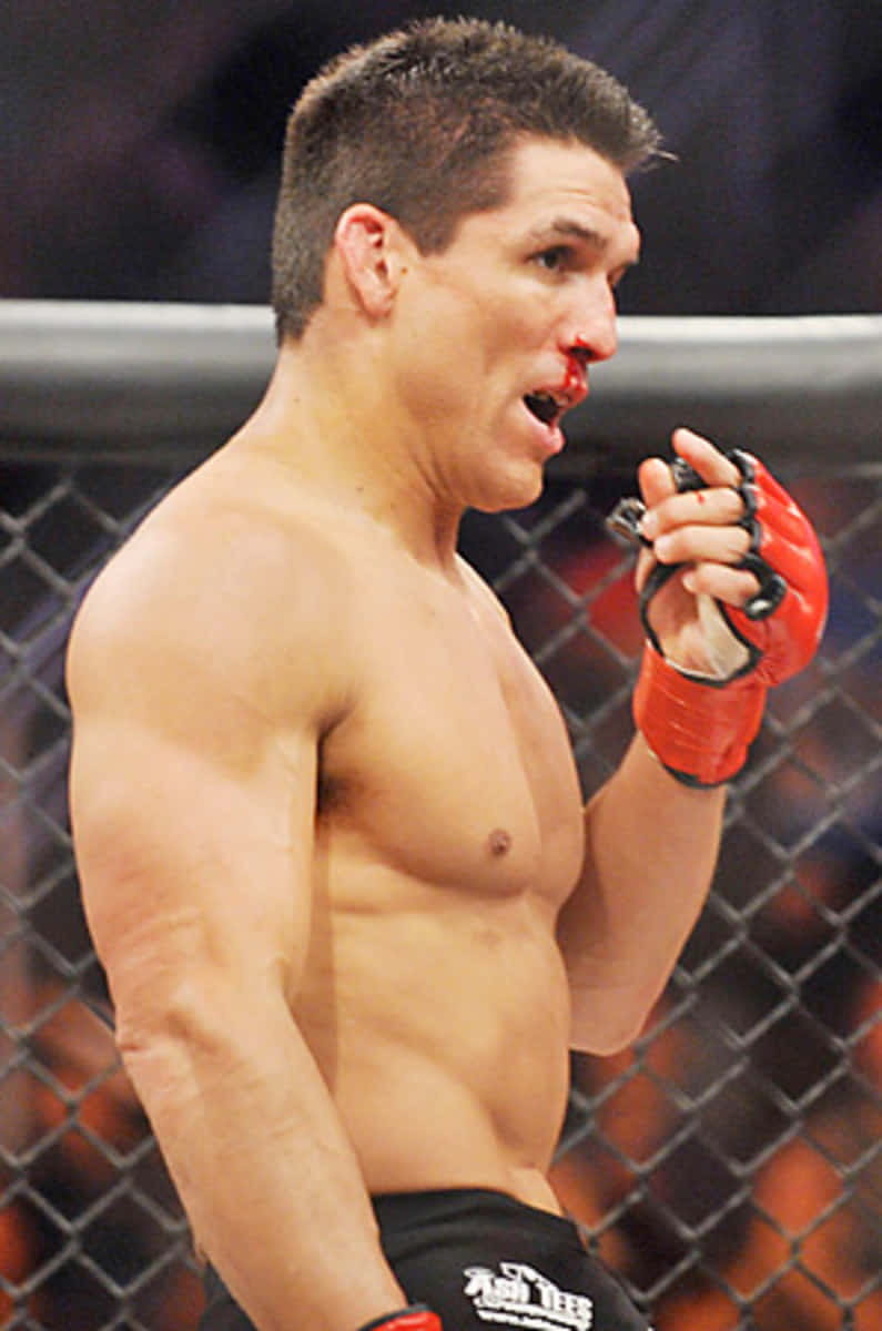 MMA 桌布 壁紙 — 一名赤裸上身、嘴唇流血、戴紅色手套的男性拳手在綜合格鬥比賽期間於籠內大喊。