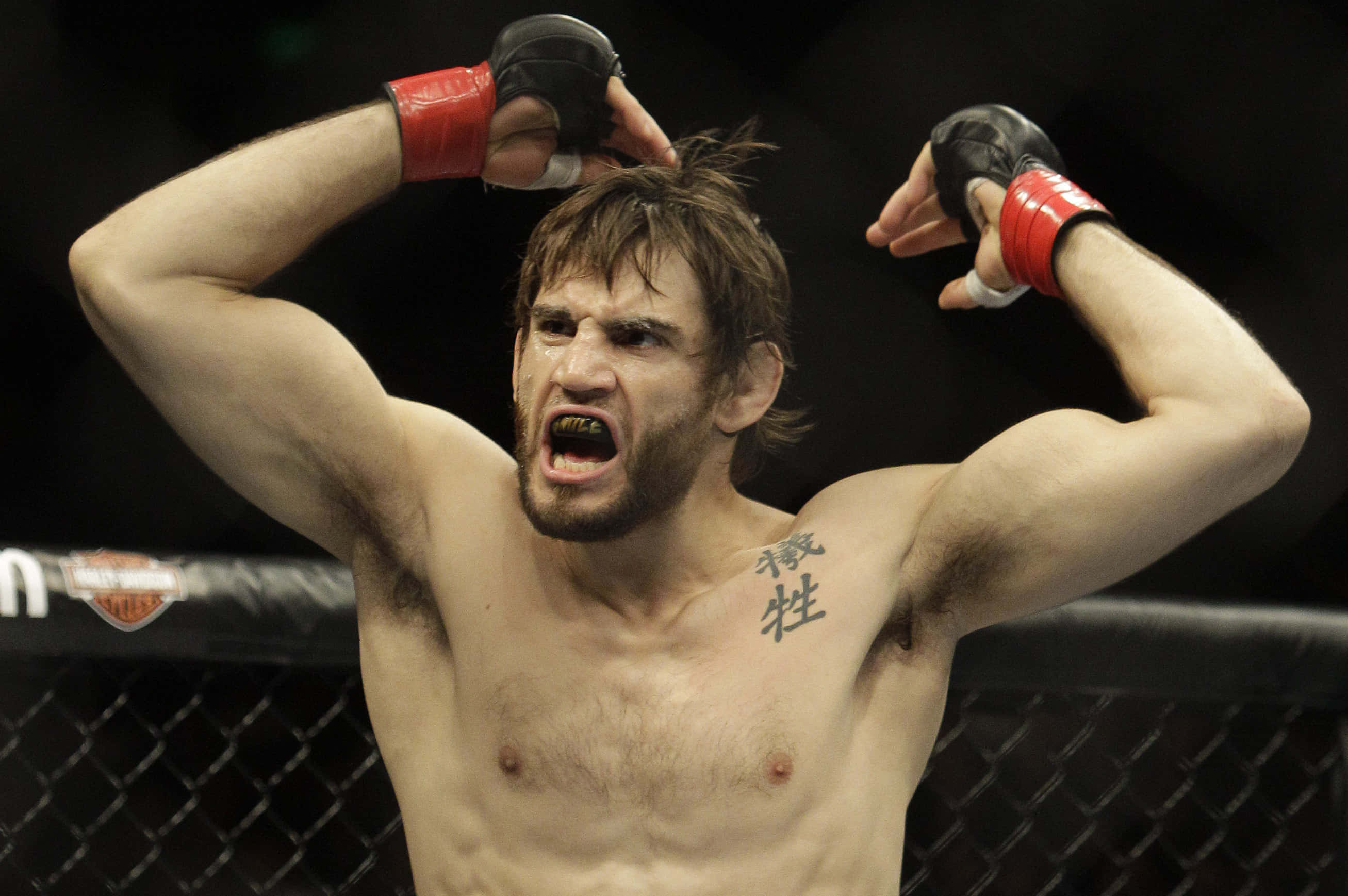 UFC 桌布 壁紙 — 一名赤裸上身、胸口有刺青的拳手在八角籠中高舉紅色手套，發出勝利的咆哮。