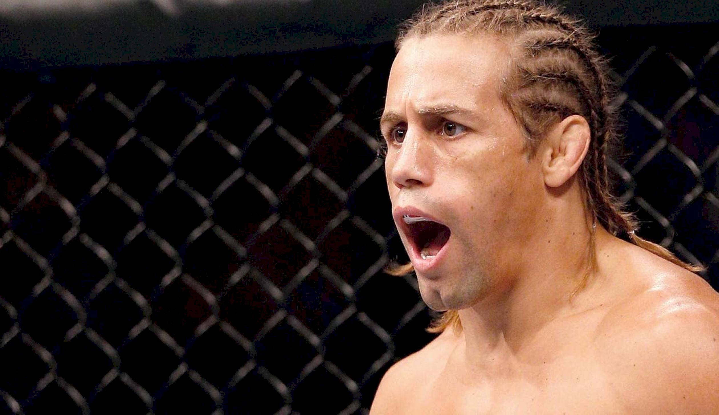UFC 桌布 壁紙 — 一名赤裸上身、辮子頭髮的鬥士在昏暗的MMA八角籠內猛烈咆哮。