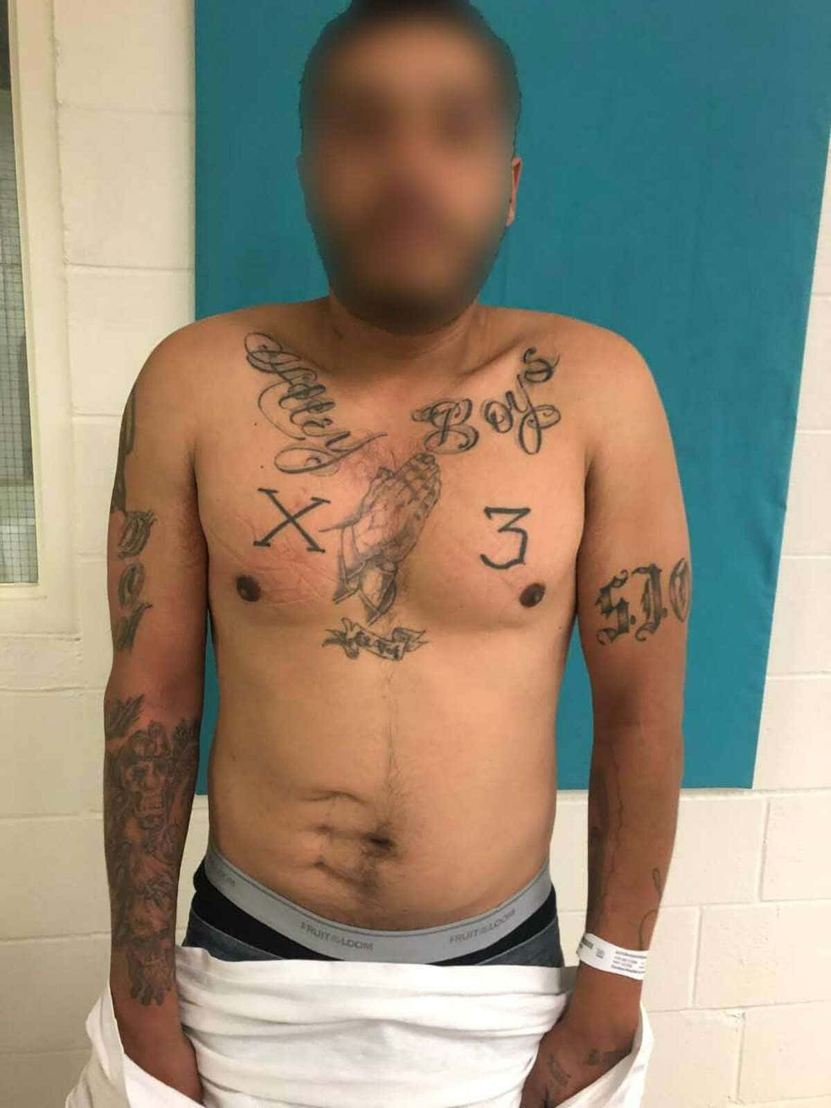 Sur 13 桌布 壁紙 — 一名赤裸上身、面容模糊的男子站在藍色牆壁前，展示包括 'Baby Boy's X 3' 和骷髏圖案在內的大量刺青。