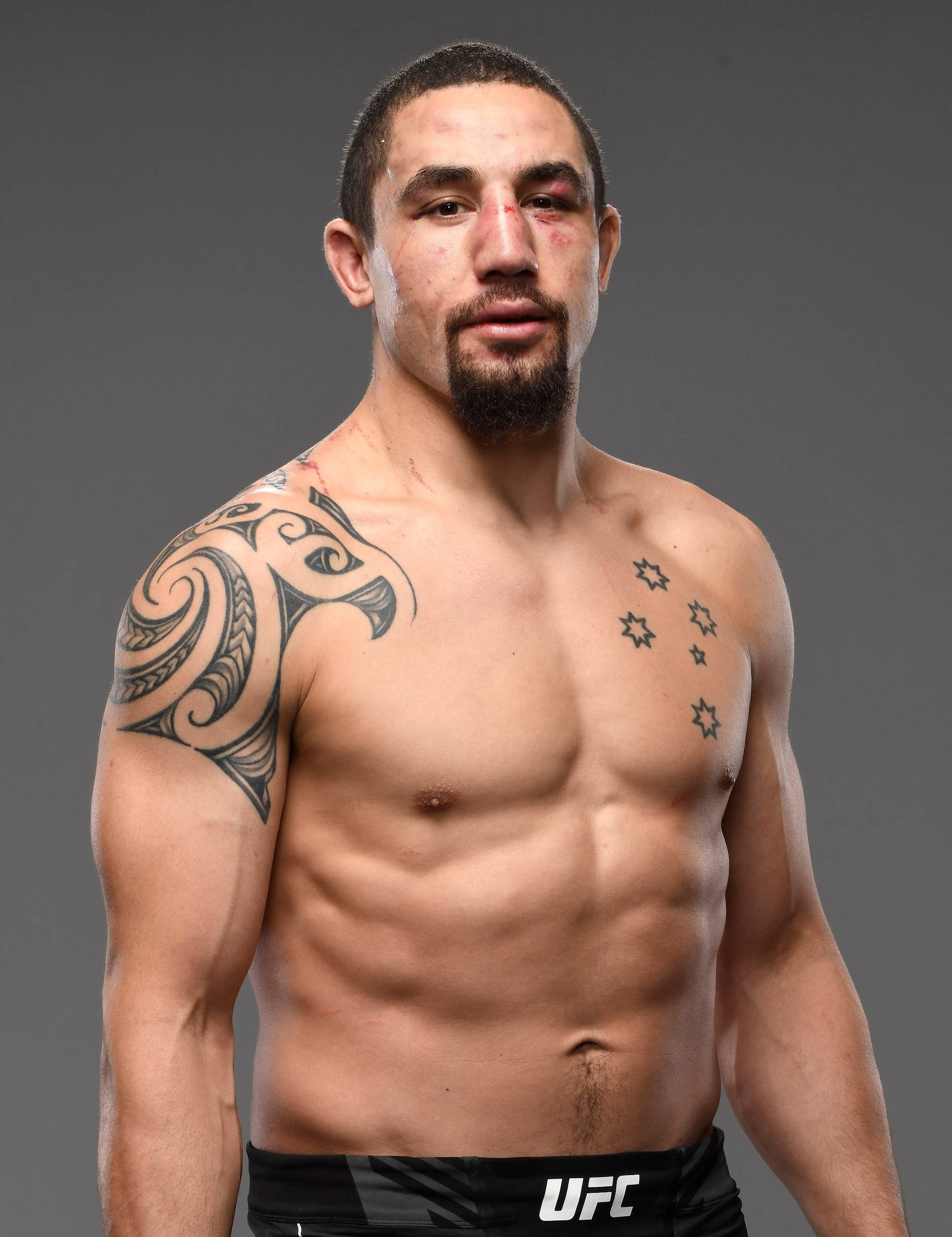 運動 桌布 壁紙 — 一名赤裸上身的UFC拳手，肩上有一個部落紋身，胸前有星星，站在灰色背景前，眼睛瘀傷。