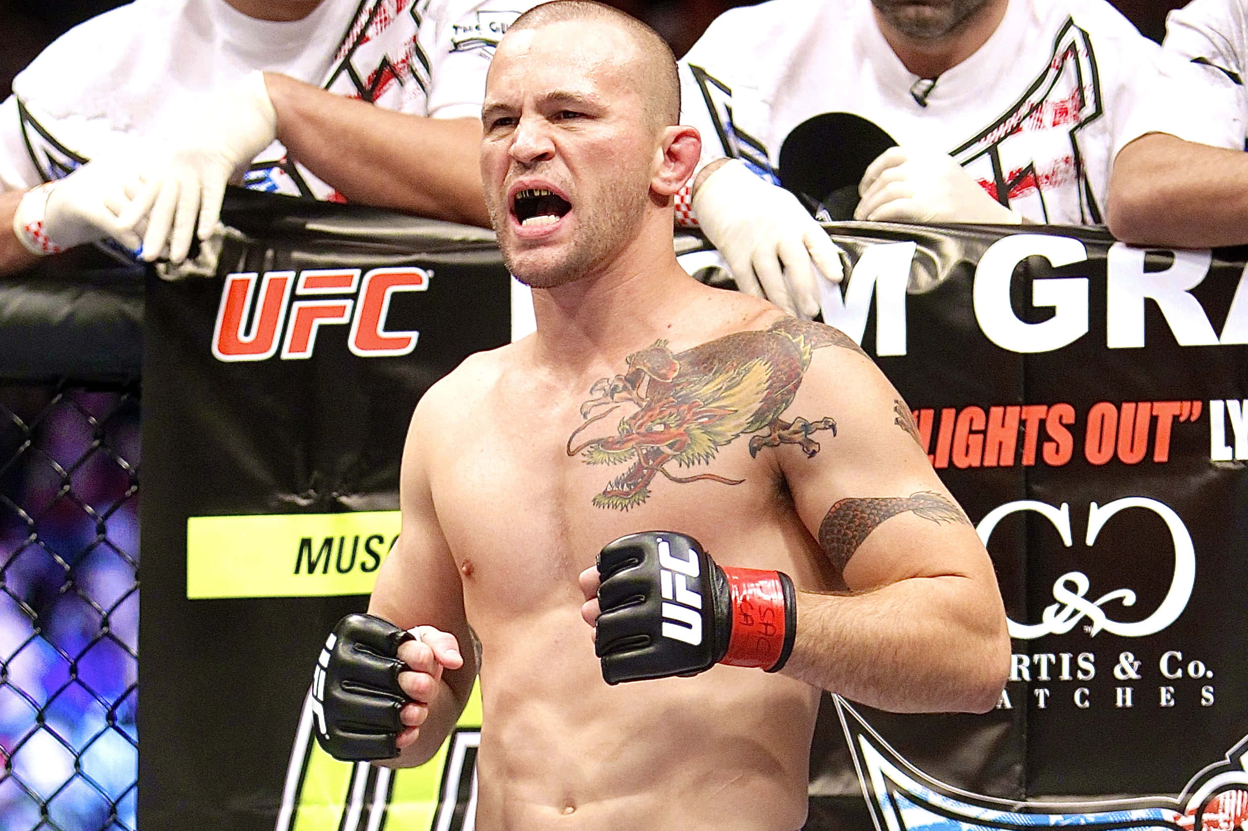 UFC 桌布 壁紙 — 一名赤裸上身的UFC拳手，身上有龍紋身，在八角籠內勝利咆哮，身後有粉絲歡呼。