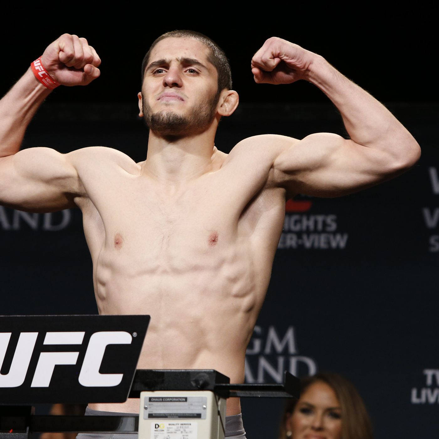 UFC 桌布 壁紙 — 一名赤裸上身的UFC拳手在明亮的場館燈光下，於體重磅上展示其肌肉發達的手臂。