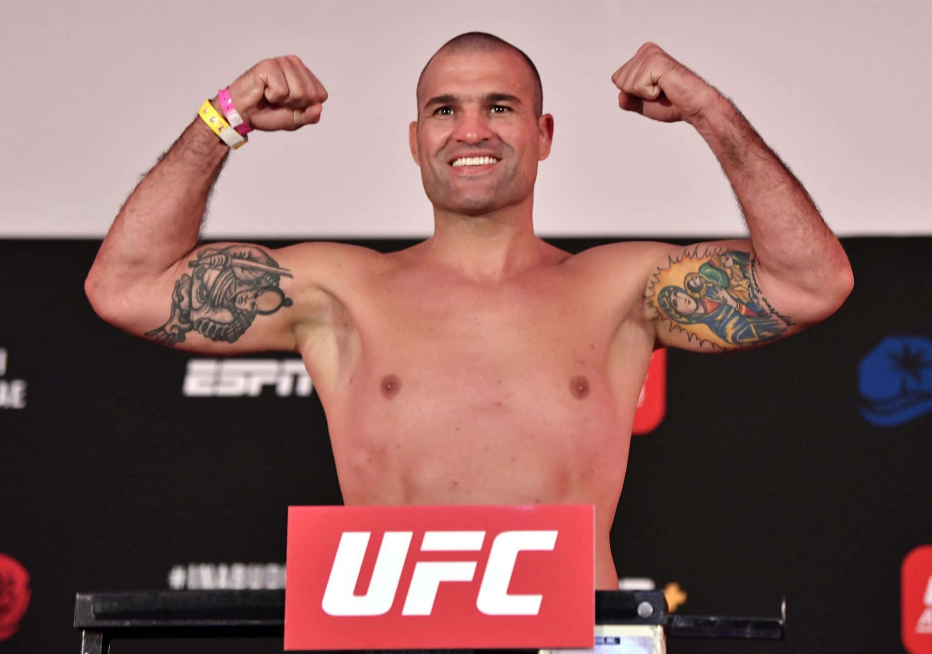 Champion 桌布 壁紙 — 一名赤裸上身的UFC拳手在稱重活動中站在體重磅上，雙臂彎曲，紋身清晰可見。