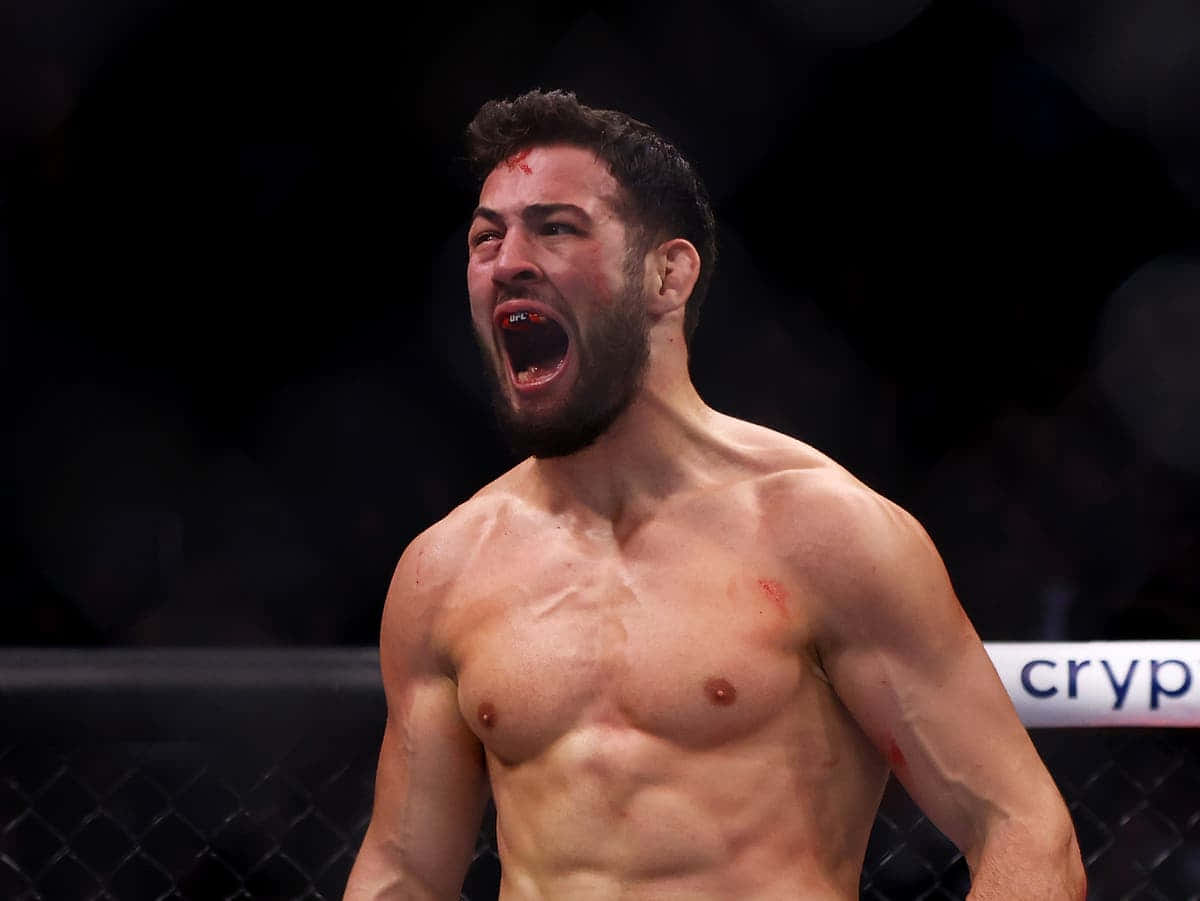 UFC 桌布 壁紙 — 一名赤裸上身的戰士，臉上和胸口沾滿鮮血，在昏暗的八角籠內發出勝利的咆哮。