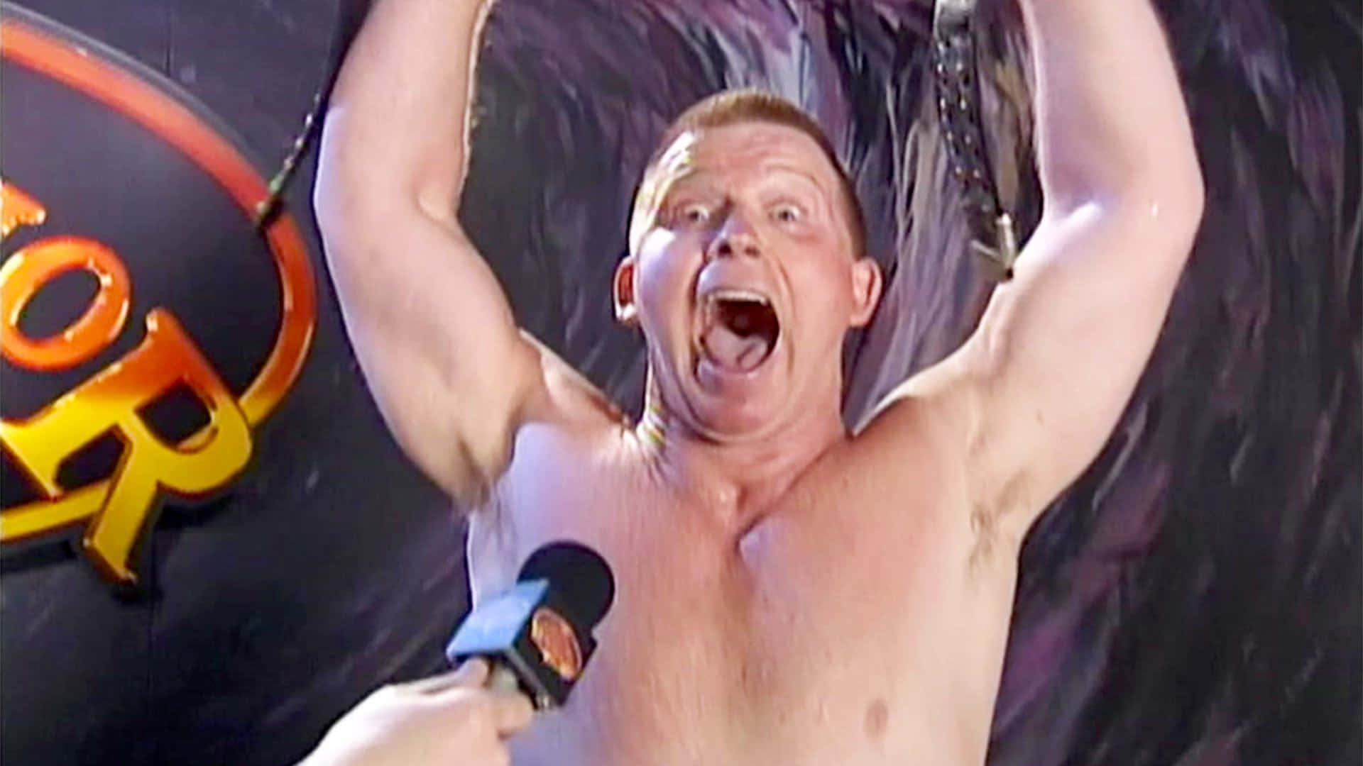 WWE 桌布 壁紙 — 一名赤裸上身的摔角手在黑暗背景下，當麥克風靠近他時，高舉雙臂勝利地吶喊。