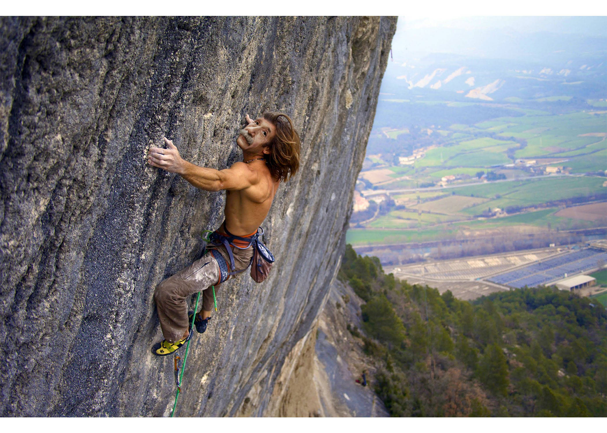 Climbing 桌布 壁紙 — 一名赤裸上身的攀岩者攀爬陡峭的岩壁，下方是廣闊的綠色山谷和太陽能農場。