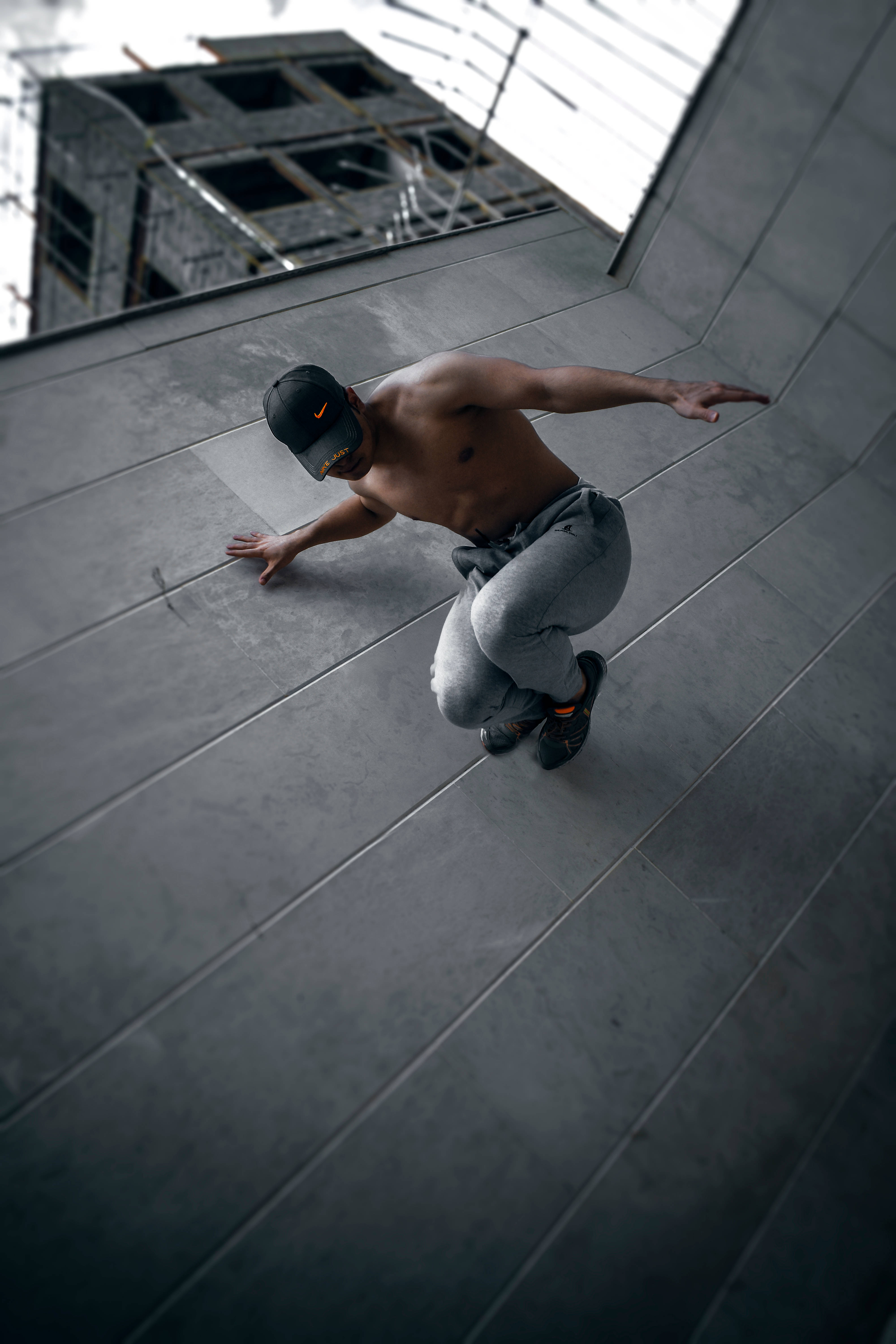 Parkour 桌布 壁紙 — 一名赤裸上身的男子穿著灰色運動褲和帽子，蹲在混凝土屋頂上，背景是建築工地。
