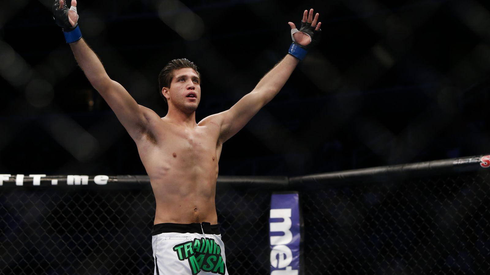 Brian Ortega 桌布 壁紙 — 一名赤裸上身的男性拳手在昏暗的MMA八角籠內勝利地高舉雙臂。