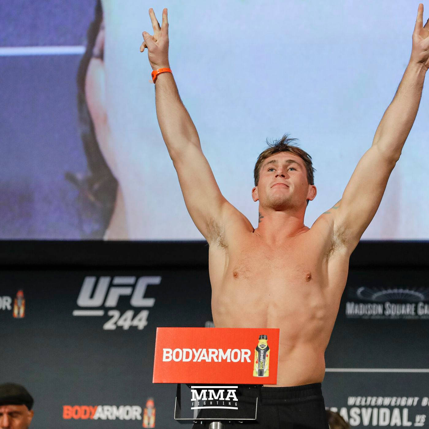 UFC 桌布 壁紙 — 一名赤裸上身的男拳手在UFC 244稱重活動中高舉雙臂慶祝勝利，身後有一個大螢幕。
