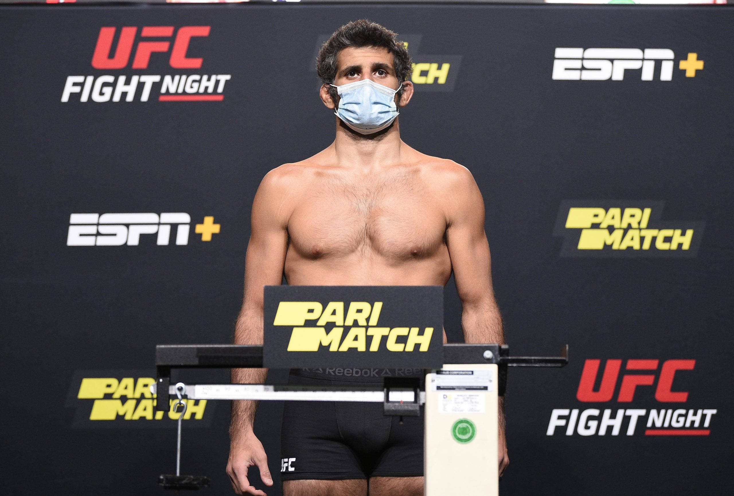 UFC 桌布 壁紙 — 一名赤裸上身的男拳手戴著口罩，在UFC格鬥之夜的稱重活動中站在體重磅上。