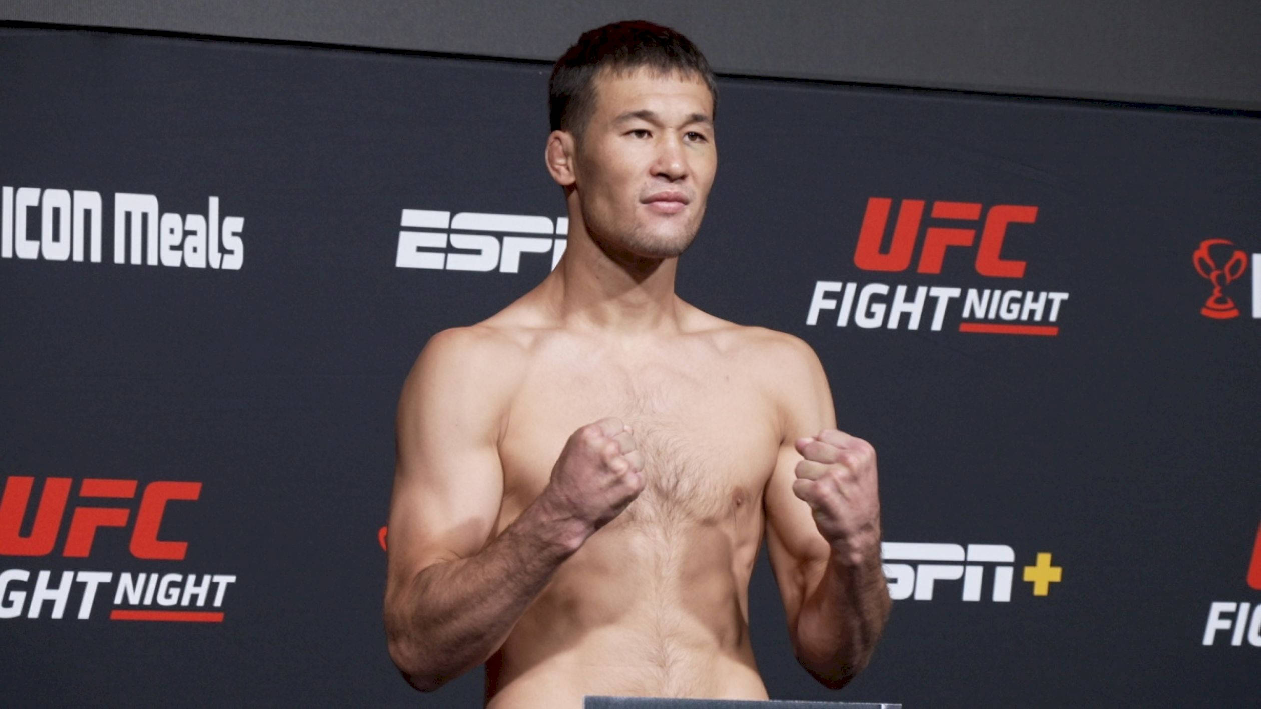 UFC 桌布 壁紙 — 一名赤裸上身的男拳手自信地站立，拳頭高舉，背景是UFC Fight Night品牌標誌。