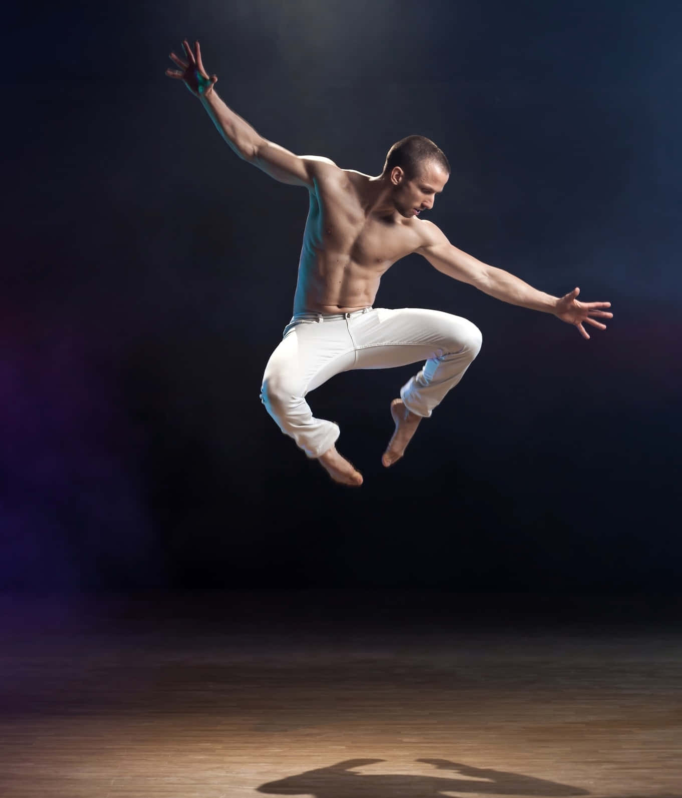 dancer 桌布 壁紙 — 一名赤裸上身的男舞者在白色褲子中於黑暗的攝影棚背景下，在戲劇性的燈光中騰空跳躍。