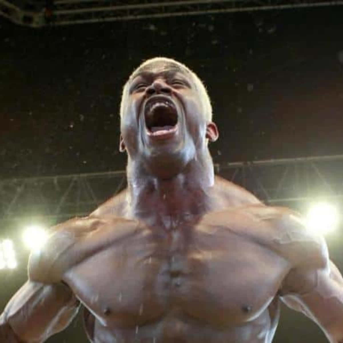 UFC 桌布 壁紙 — 一名赤裸上身的肌肉男在明亮的場館燈光下，汗水在空中飛濺，帶著強烈情緒吶喊。