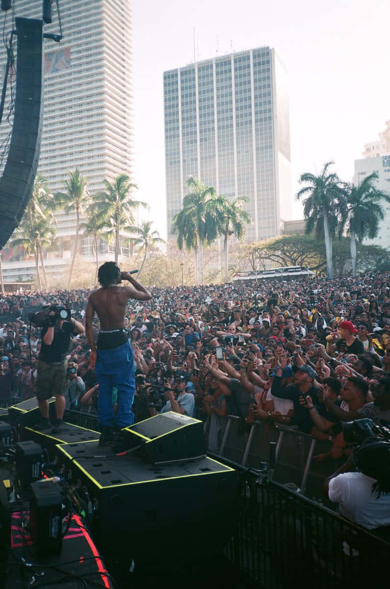 Pierre Bourne 桌布 壁紙 — 一名赤裸上身的表演者在發光的舞台喇叭上對著麥克風唱歌，大量人群在明亮的日光下歡呼。