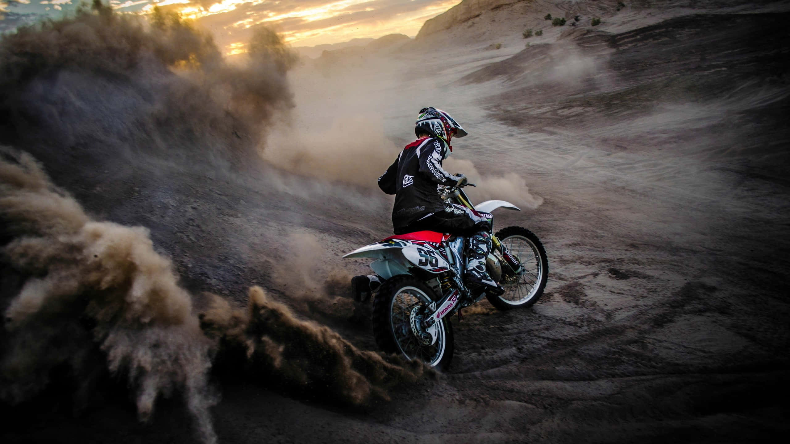 Motocross 桌布 壁紙 — 一名越野摩托車手在日落時分穿越塵土飛揚的沙漠峽谷，揚起巨大的沙雲。
