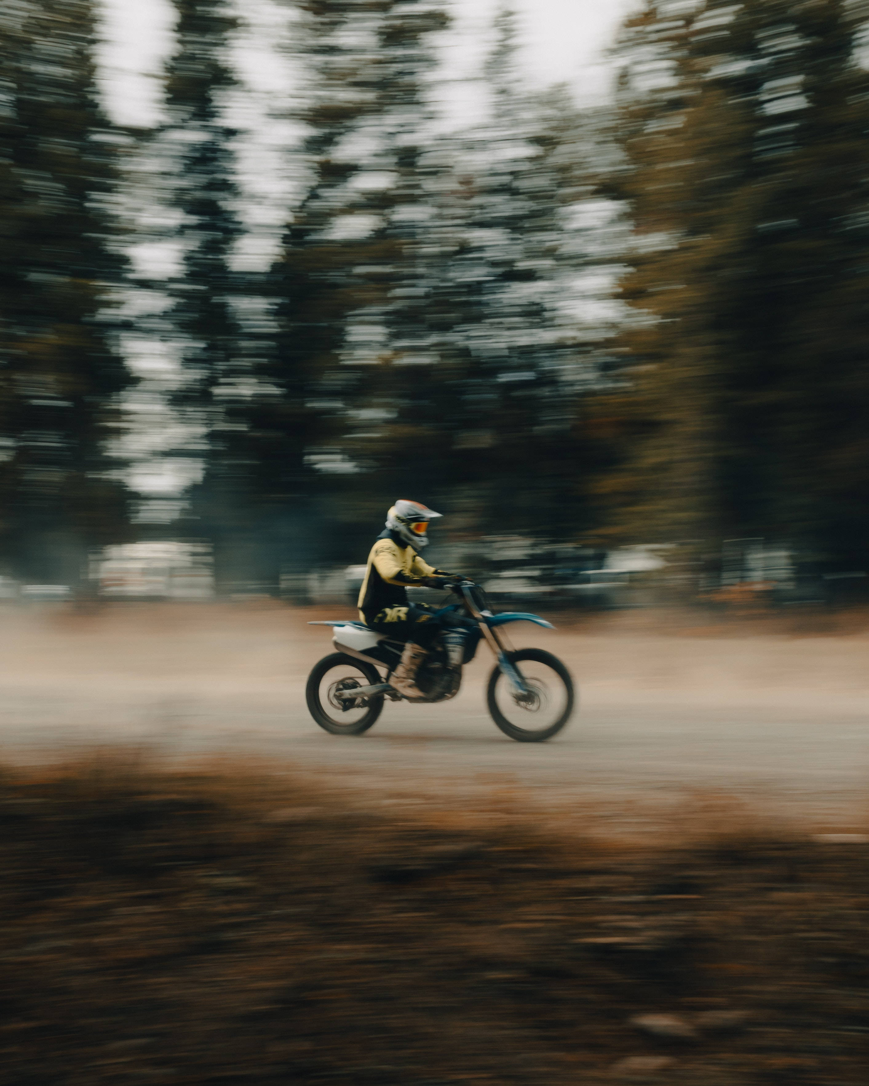Dirtbike 桌布 壁紙 — 一名越野摩托車手在森林小徑上飛馳，揚起灰塵，周圍呈現動態模糊效果。