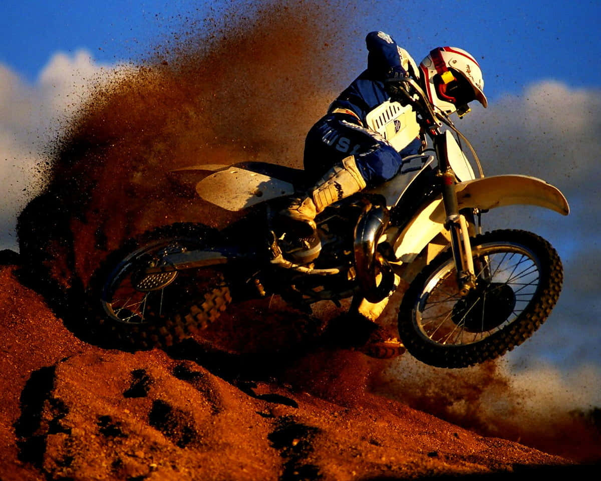 Motocross 桌布 壁紙 — 一名越野摩托車手飛越泥地跳台，在藍天下揚起一大片紅褐色塵土。