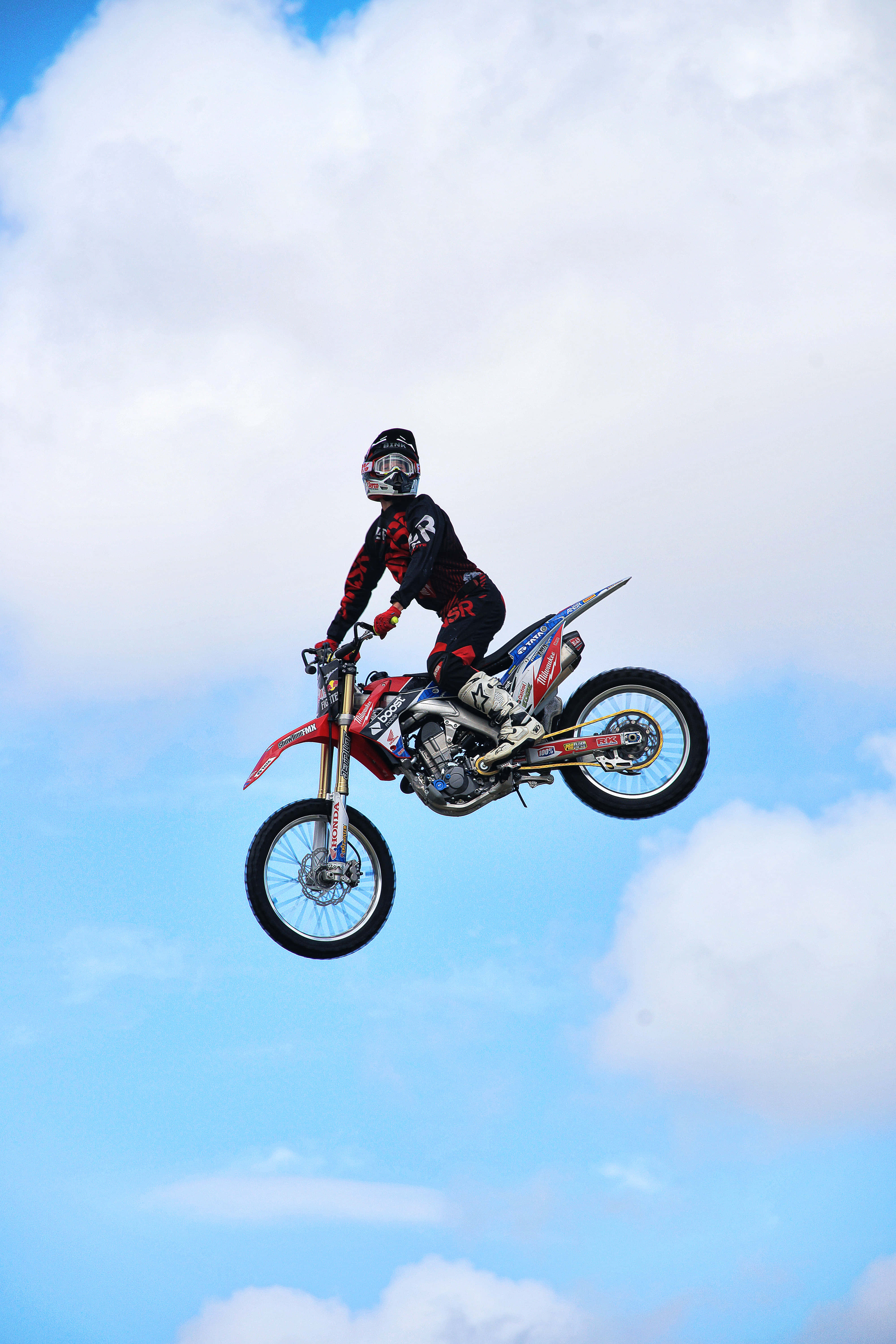 Dirtbike 桌布 壁紙 — 一名越野摩托車手騎著紅色泥地摩托車，在明亮的藍天白雲中翱翔。