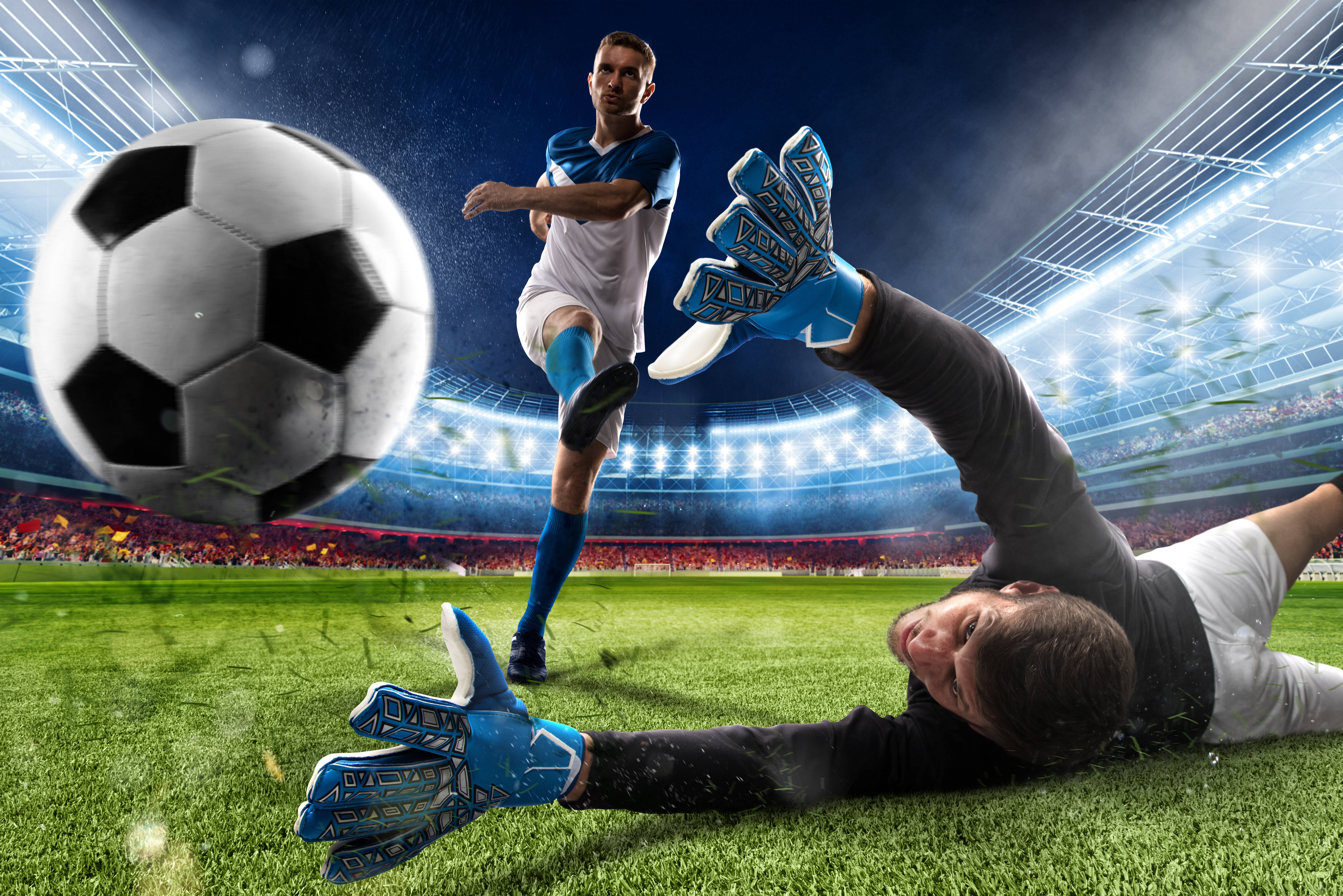 Football Field 桌布 壁紙 — 一名足球員踢球，守門員在球場燈光下撲救。