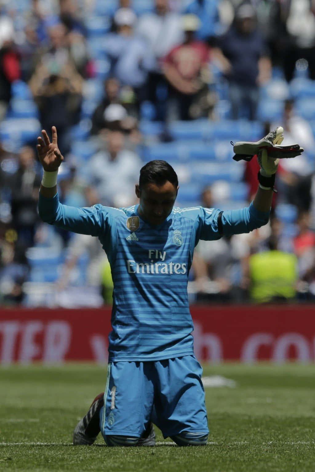 Keylor Navas 桌布 壁紙 — 一名足球守門員跪在草地上，向坐滿觀眾的體育場內的球迷高舉手套。