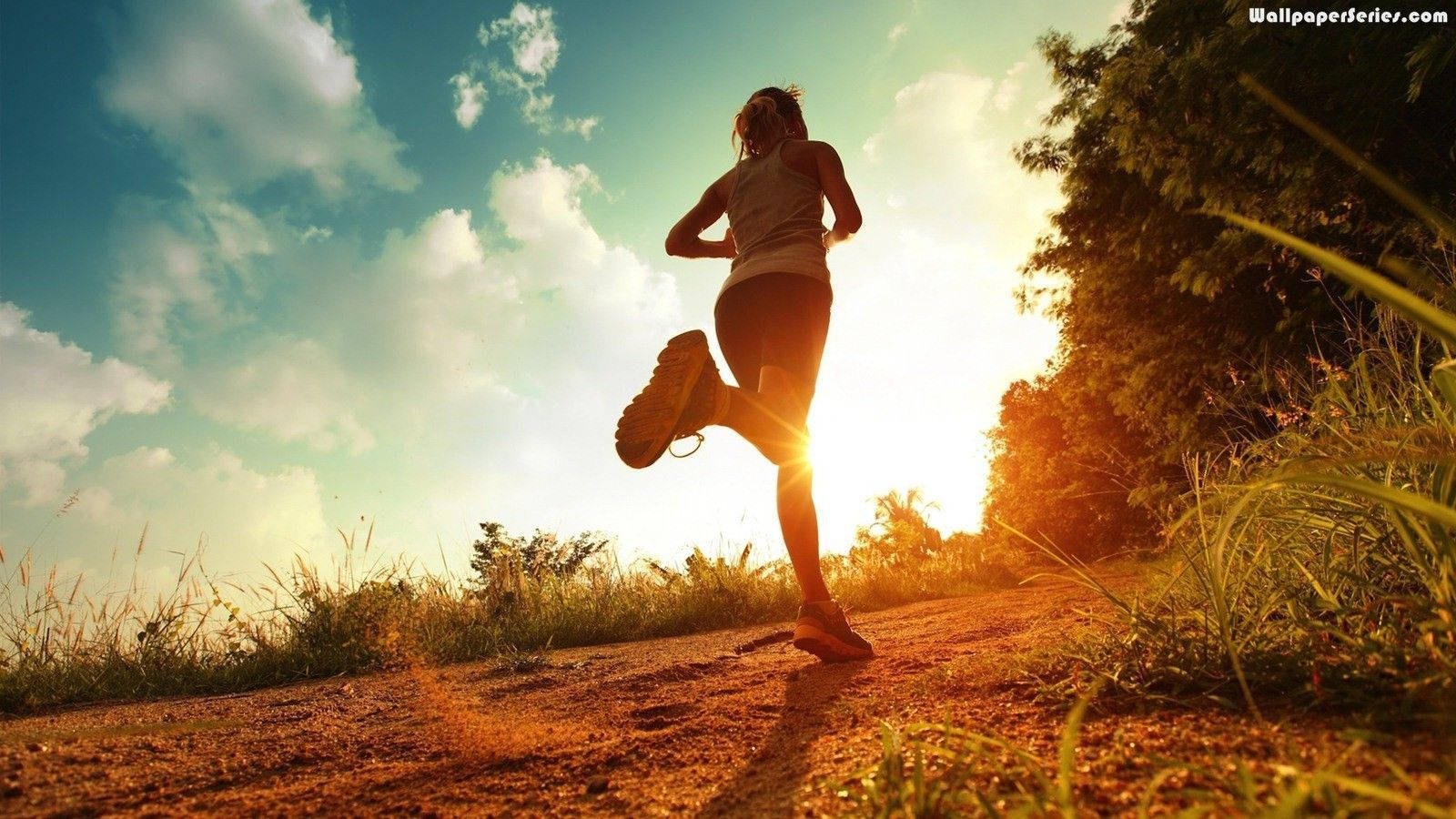 Marathon 桌布 壁紙 — 一名跑者沿著泥土小徑衝刺，金色陽光在他們身後迸發，映襯著藍天和蓬鬆的白雲。