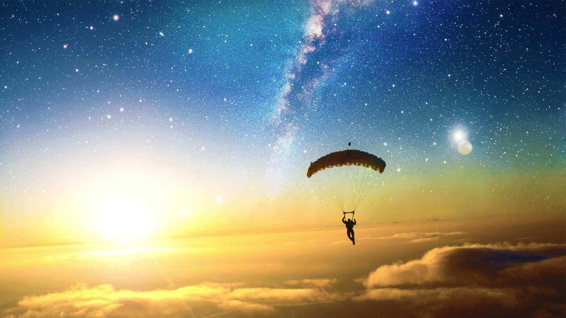 Silhouette 桌布 壁紙 — 一名跳傘運動員在 vibrant 的日落和星空下剪影，銀河拱起在頭頂。
