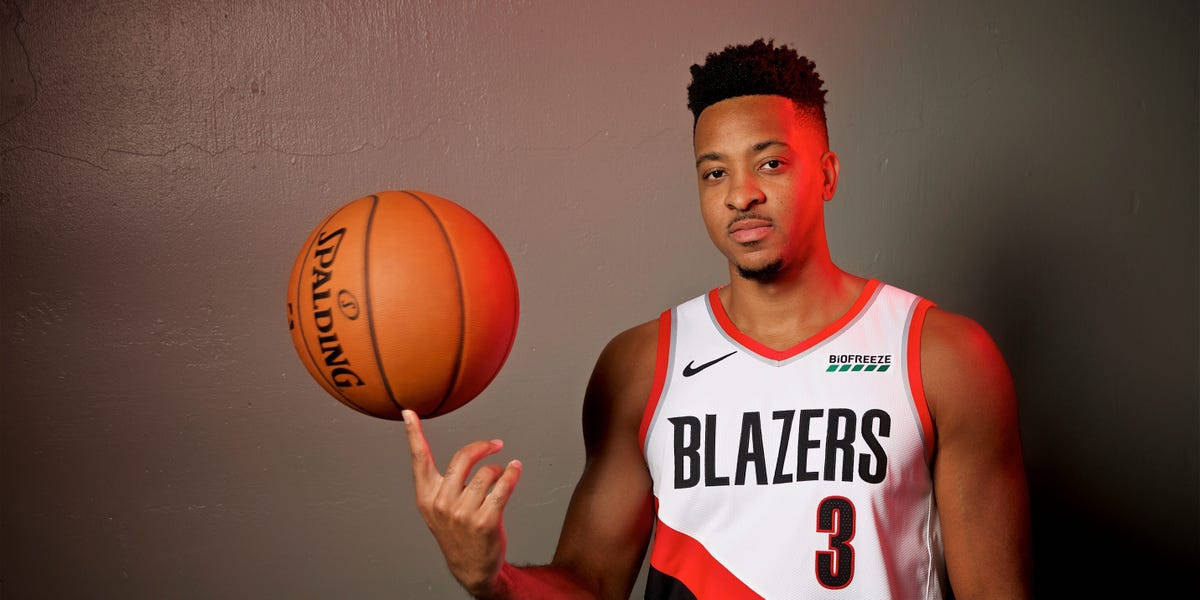 Cj 桌布 壁紙 — 一名身穿 Blazers 球衣的籃球運動員在柔和的灰色牆壁前，用指尖平衡一個橙色的 Spalding 籃球。